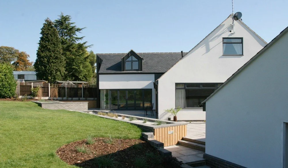 Modern house with a white exterior, large glass windows, and a garden with green grass and flower beds.