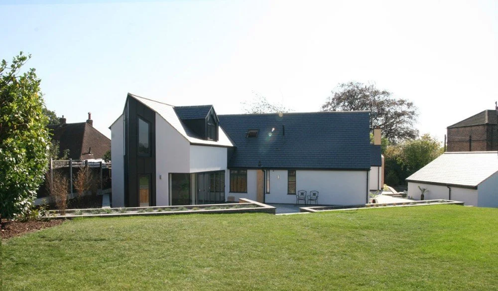 Modern house with black and white exterior, large windows, and a well-maintained lawn in a suburban neighborhood.