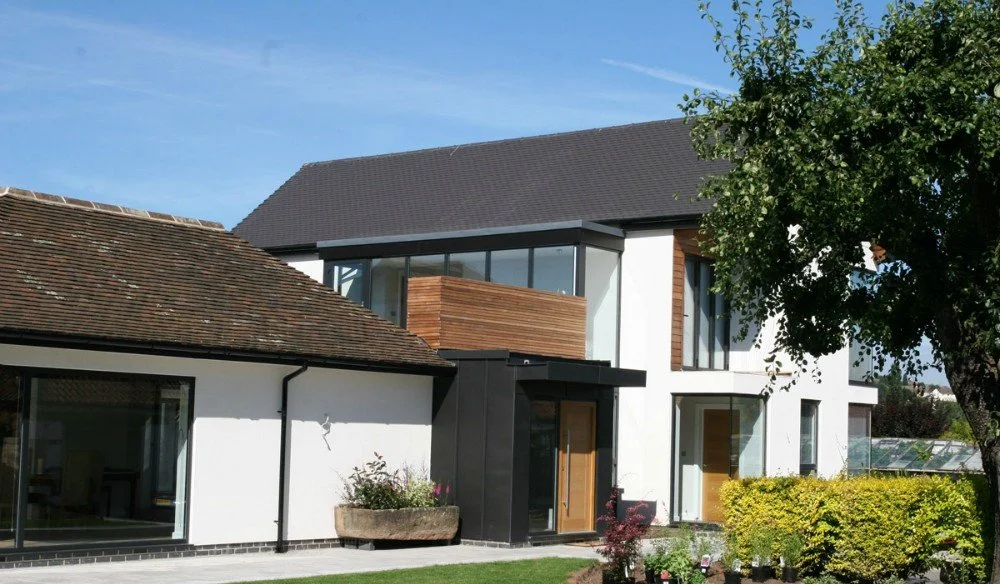 Modern white house with black and wooden accents, large glass windows, and a landscaped yard with trees and shrubs.