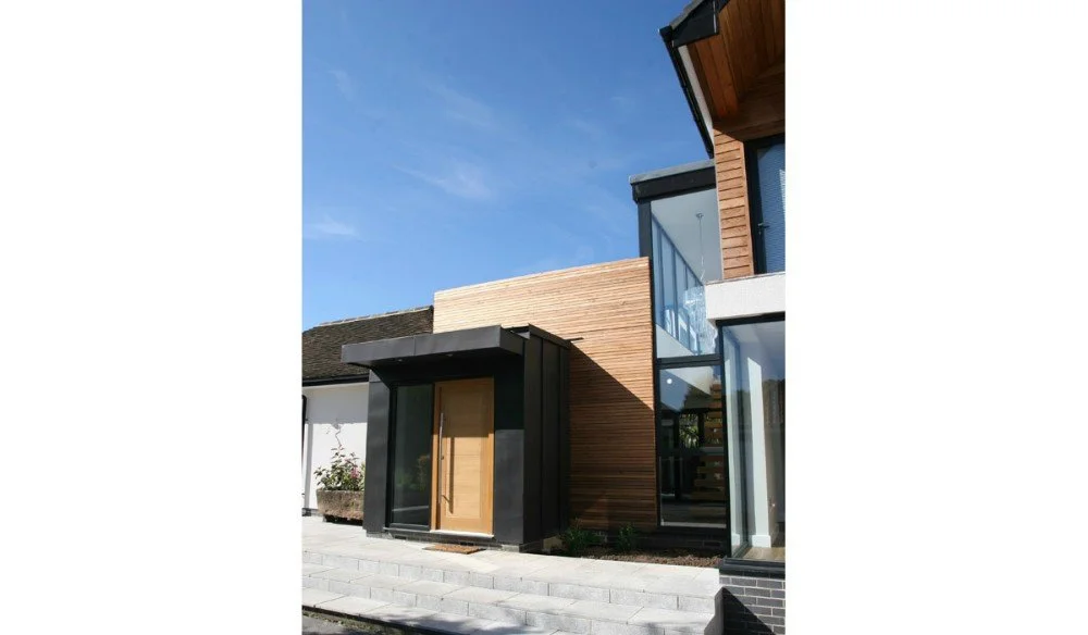 Modern residential building with a wooden door, black accents, glass walls, and a blue sky background.