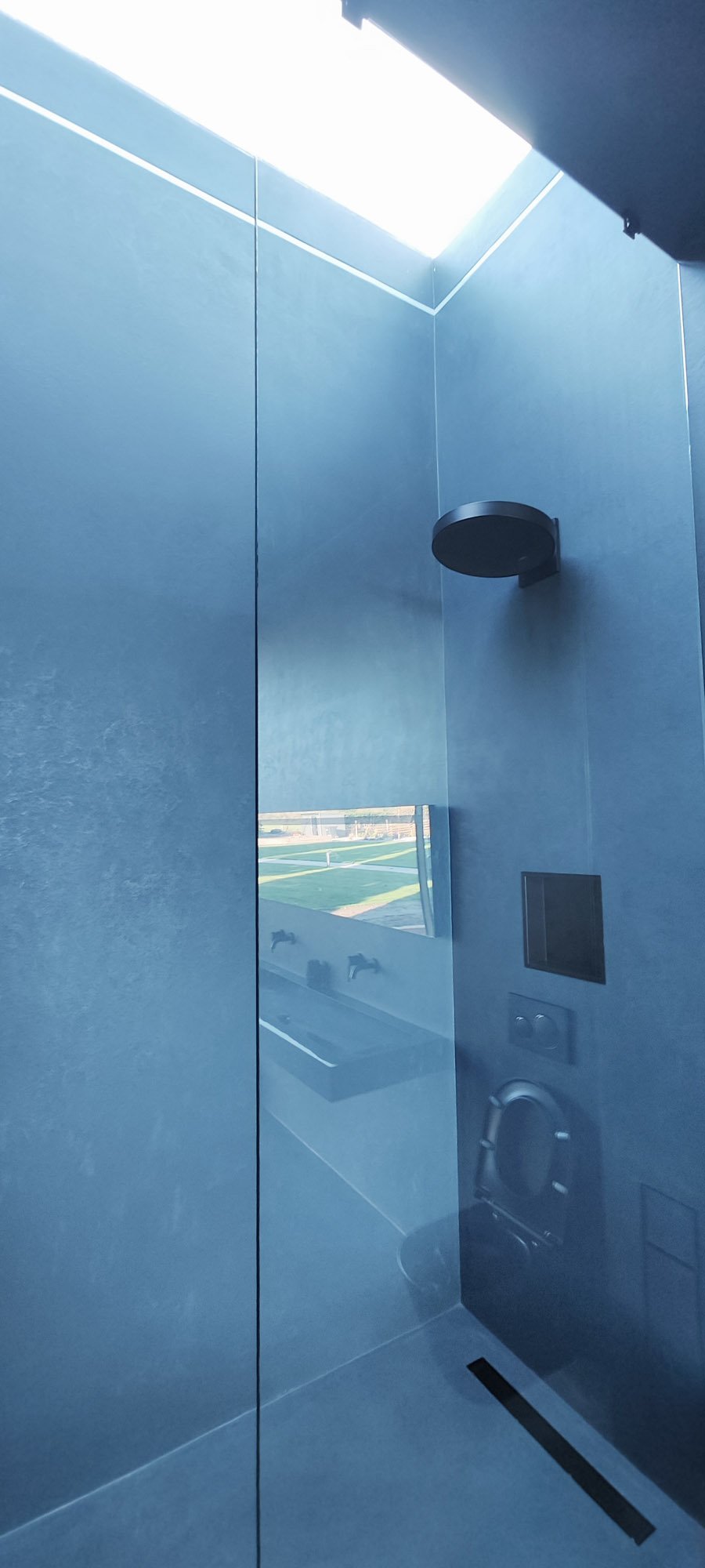 Modern shower with blue walls, a skylight, a black shower head, and a small window reflecting outdoor scenery.