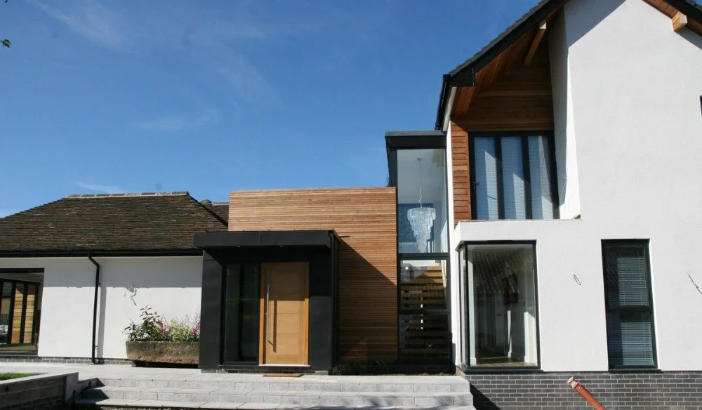 Modern house with white and wood exterior, glass staircase, and large windows under a blue sky.