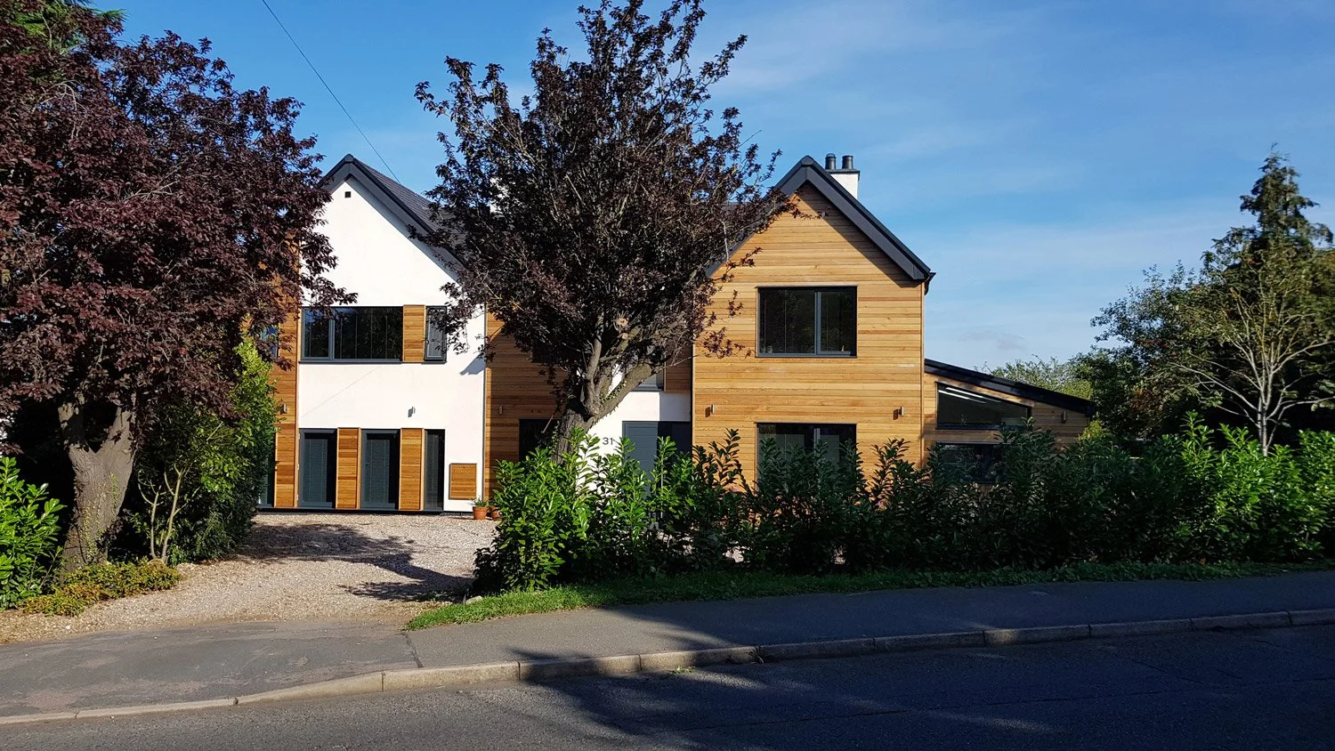 Modern house with white and wooden exterior, surrounded by trees and bushes on a sunny day