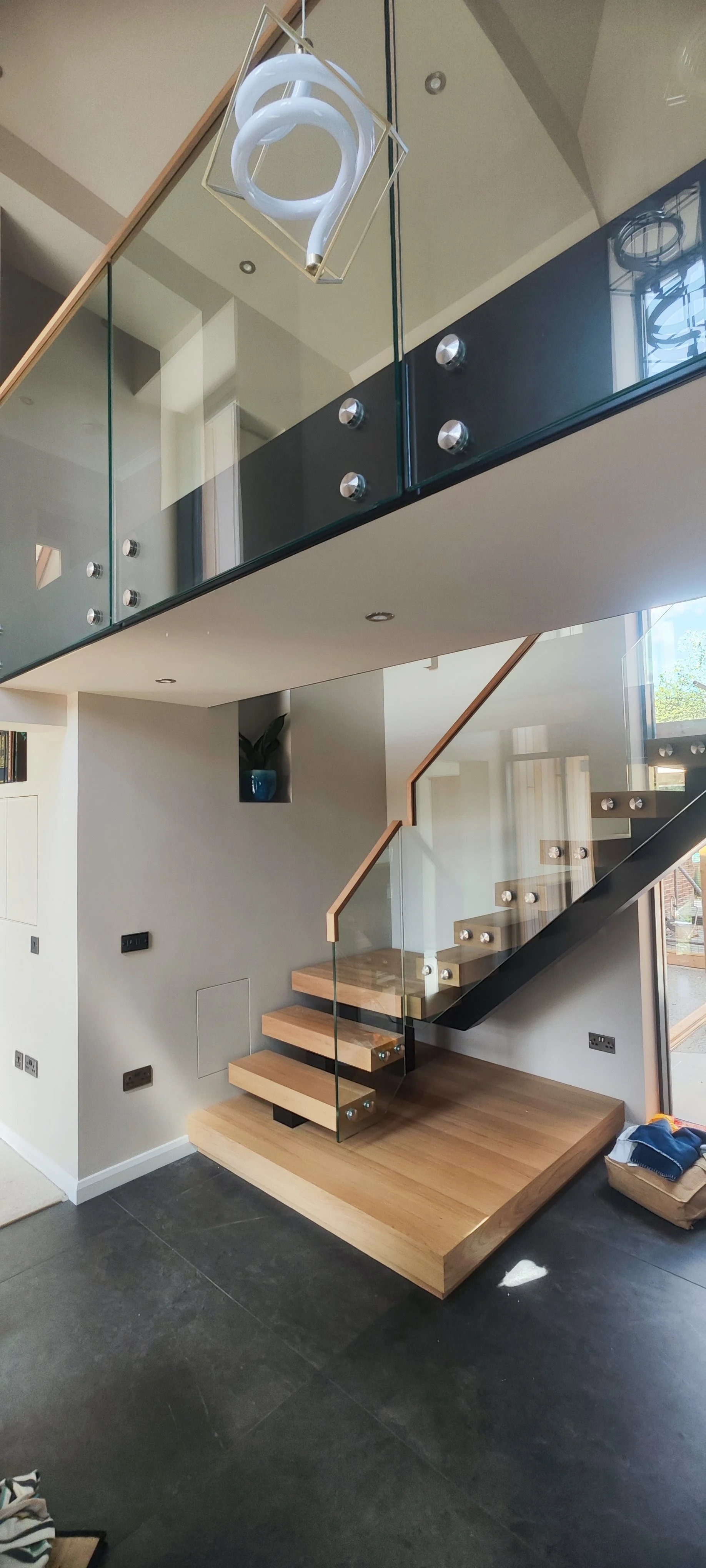 Modern staircase with wooden steps, glass railing, and black support beams inside a contemporary home.