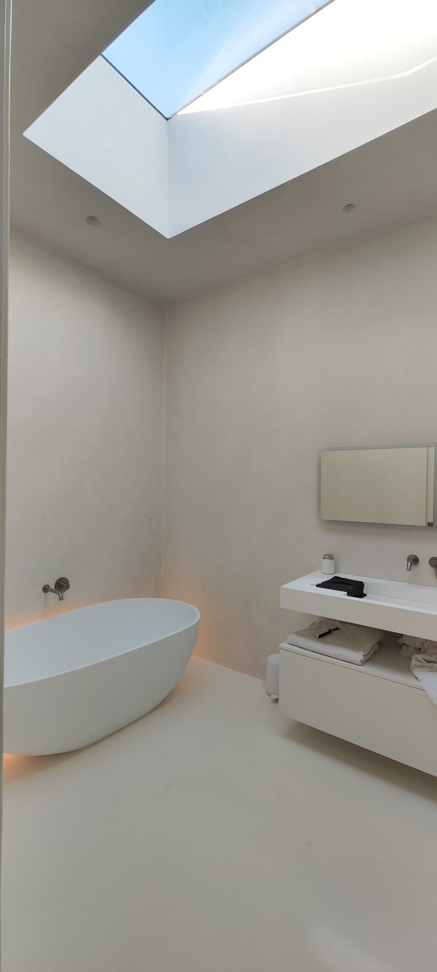 Modern bathroom featuring a white freestanding bathtub, a small white sink with a mirror above, and a skylight with a view of the sky.
