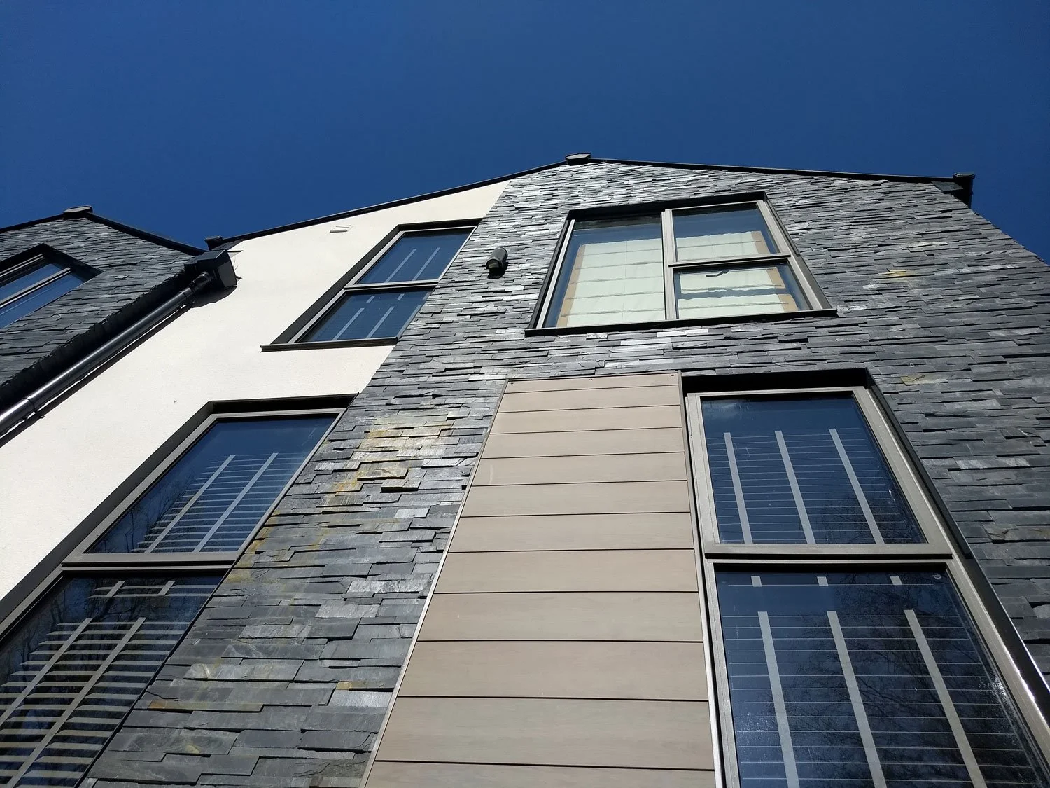 Low-angle view of a modern multi-story building with gray shingle siding and multiple windows, against a clear blue sky.