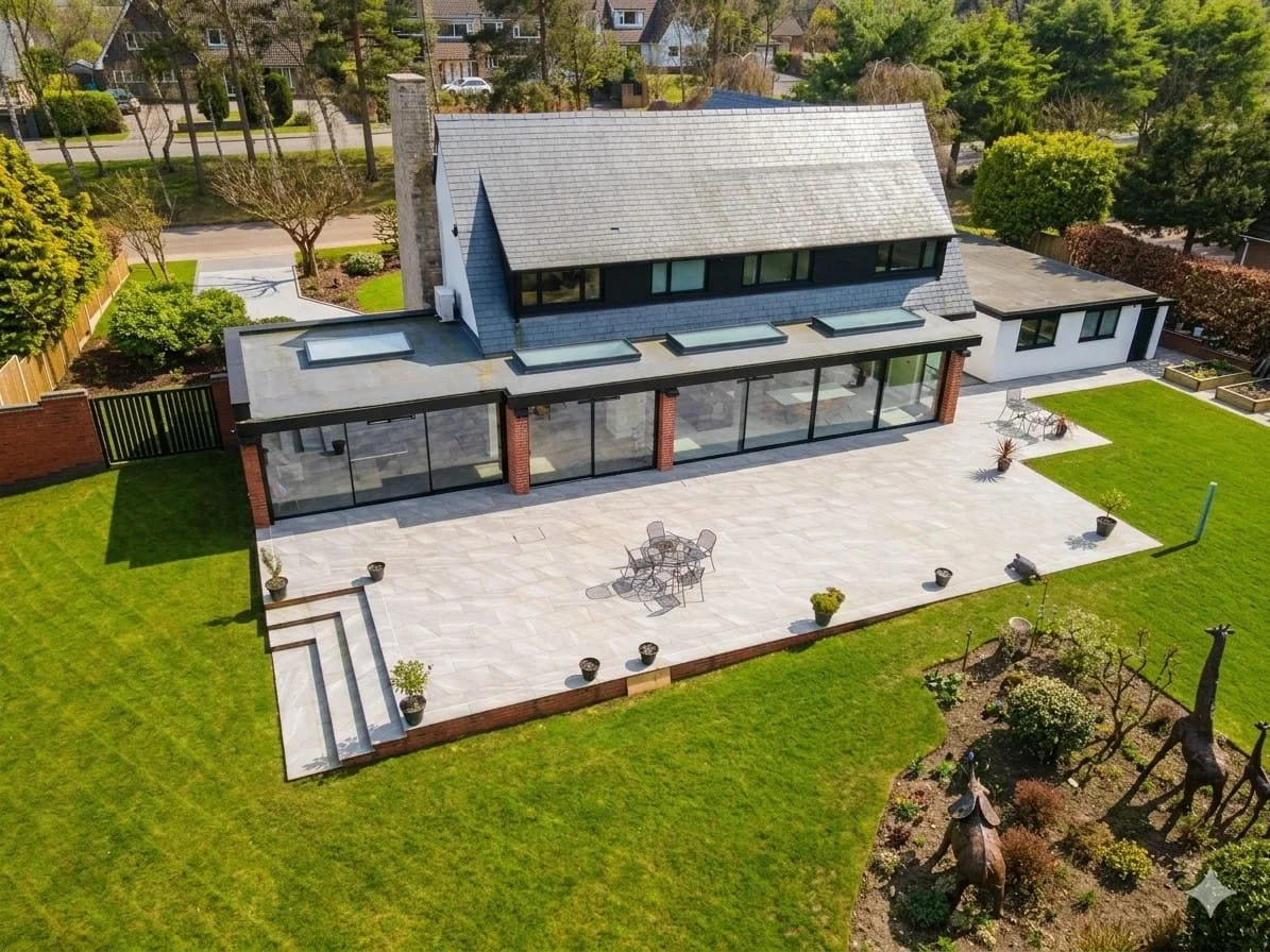 Aerial view of a modern two-story house with a spacious backyard, large patio, and green lawn, surrounded by trees and neighboring houses.