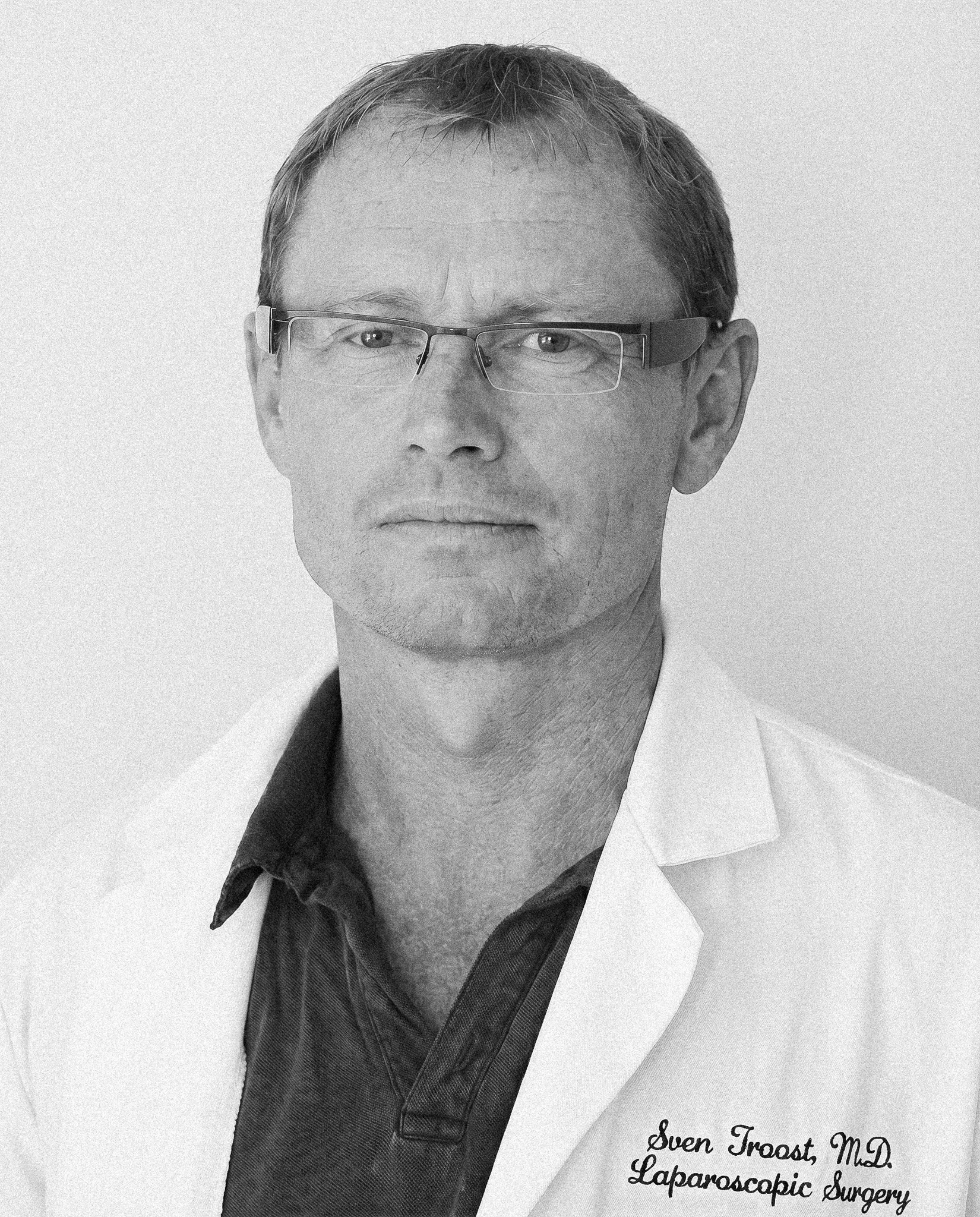 Black and white portrait of a man wearing glasses, dressed in a business shirt and tie, with a white coat. Text on the coat reads 'Sven Troost, Md. Laparoscopic Surgery'.
