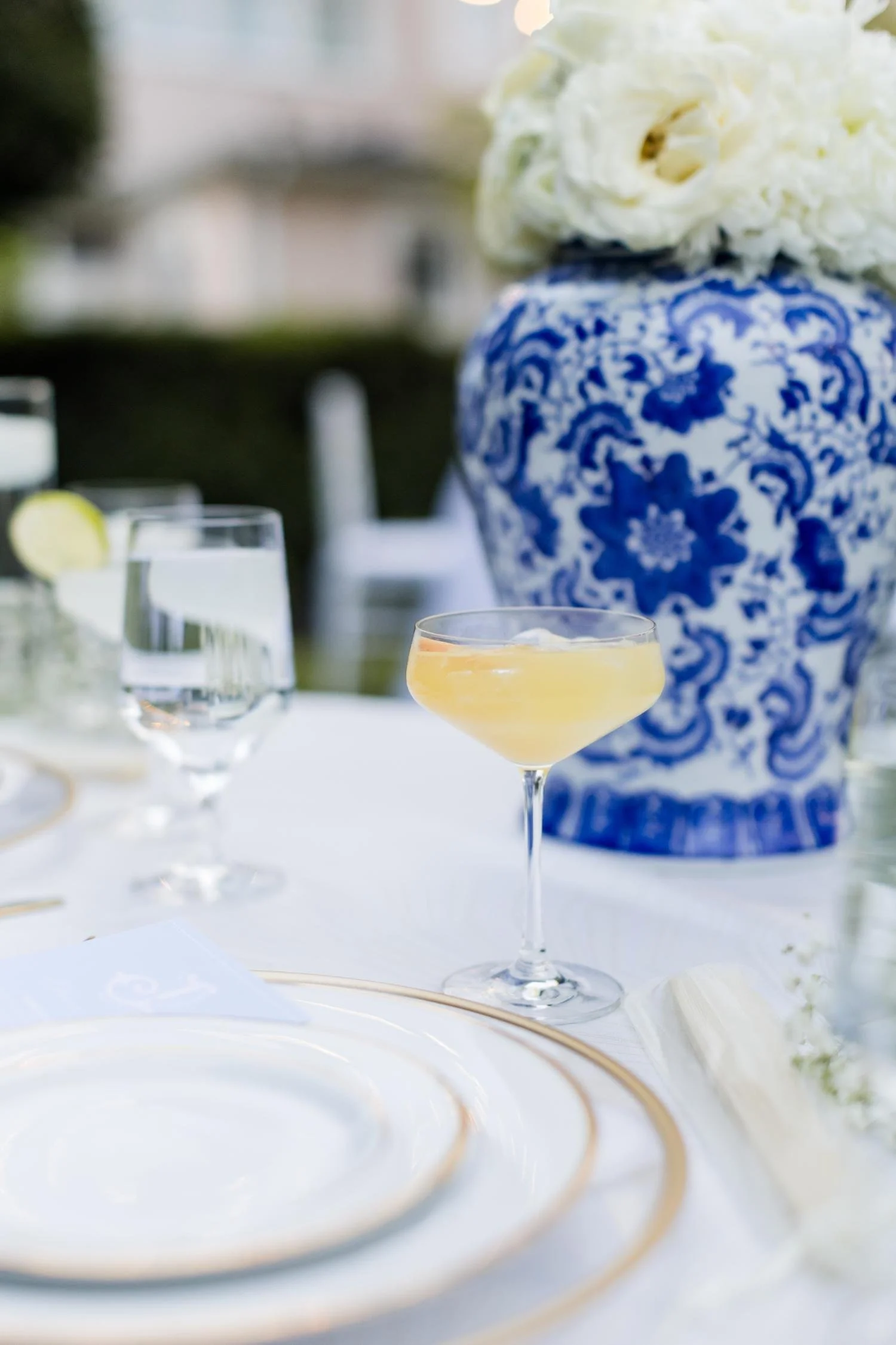 An elegant outdoor table setting with glassware and a floral centerpiece in a blue and white vase.