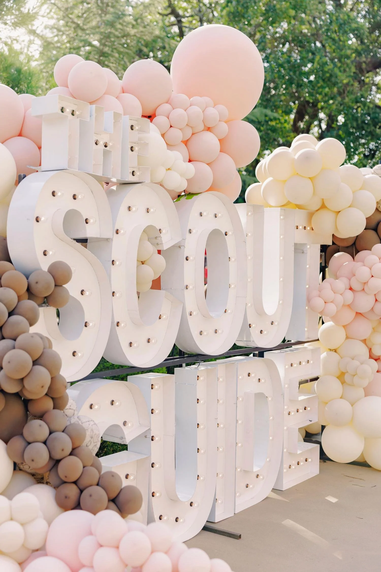 Large white illuminated sign spelling 'LOVE' surrounded by pink, white, and beige balloons outdoors.