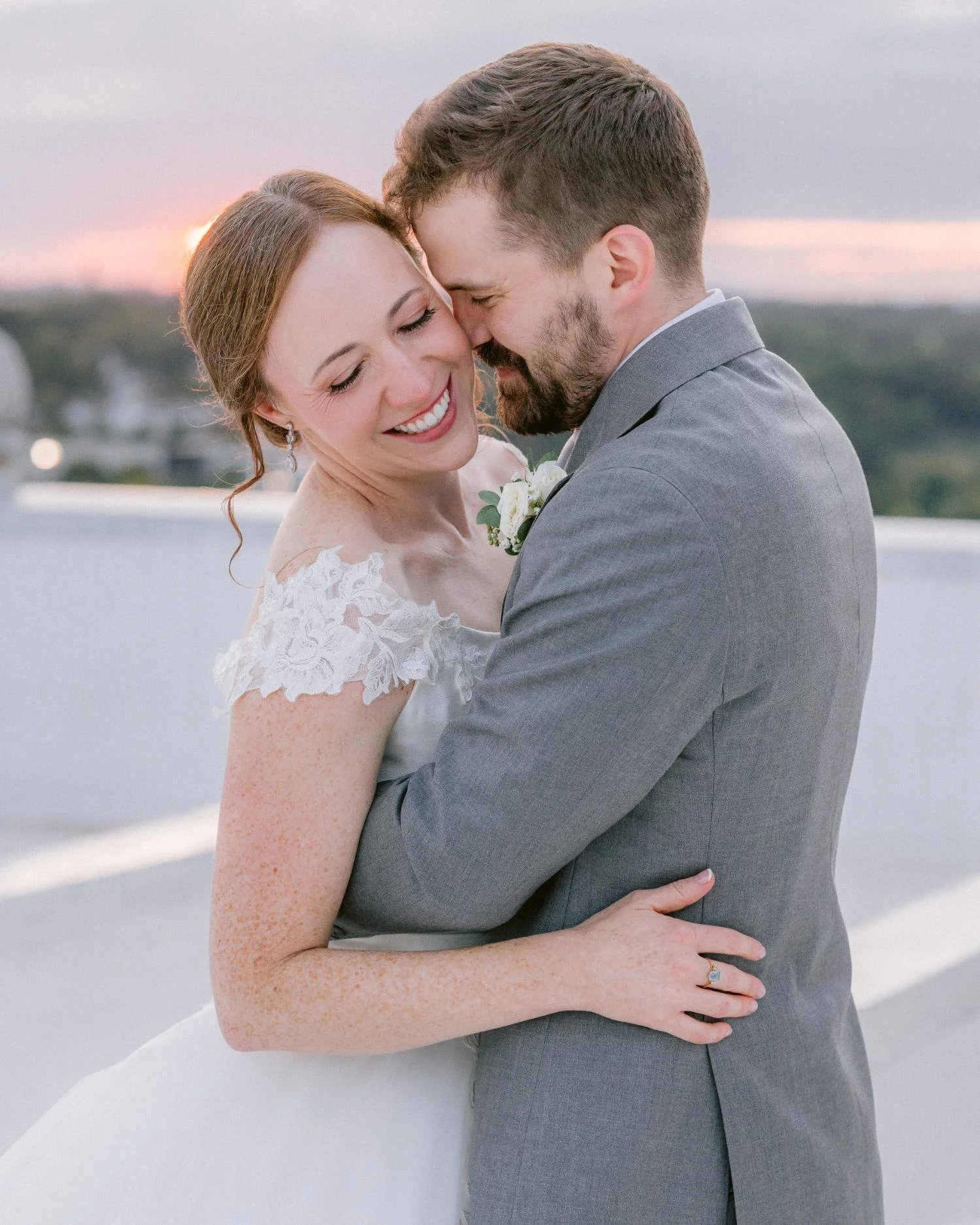 A bride and groom smiling and embracing outdoors during sunset.