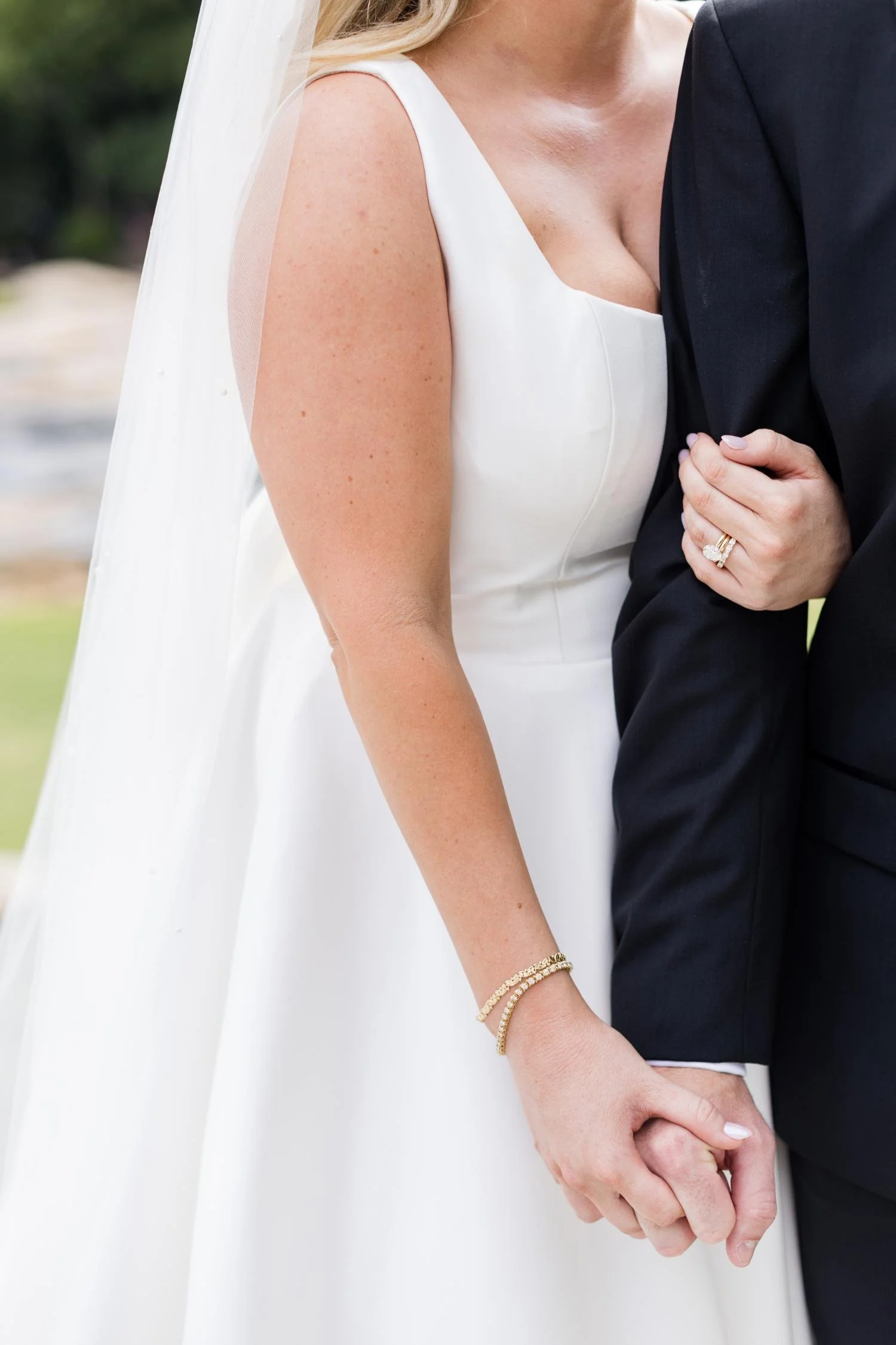 Close-up of a bride and groom holding hands during a wedding, with the bride wearing a white dress and jewelry, and the groom in a dark suit.
