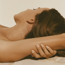 A woman lies on her back with her arms extended behind her head, relaxed.