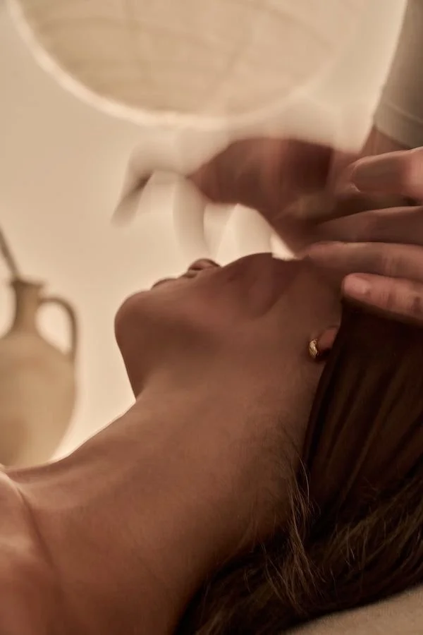 A woman lying down with her eyes closed, holding a white coffee mug near her face in a relaxed setting.