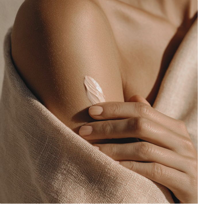 Close-up of a person's arm with a dab of light pink lotion on the skin, next to folded beige fabric.