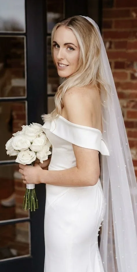 A classic bridal portrait featuring a romantic, monochromatic bouquet of full-bodied white roses. The soft textures of the blooms perfectly complement the gown.