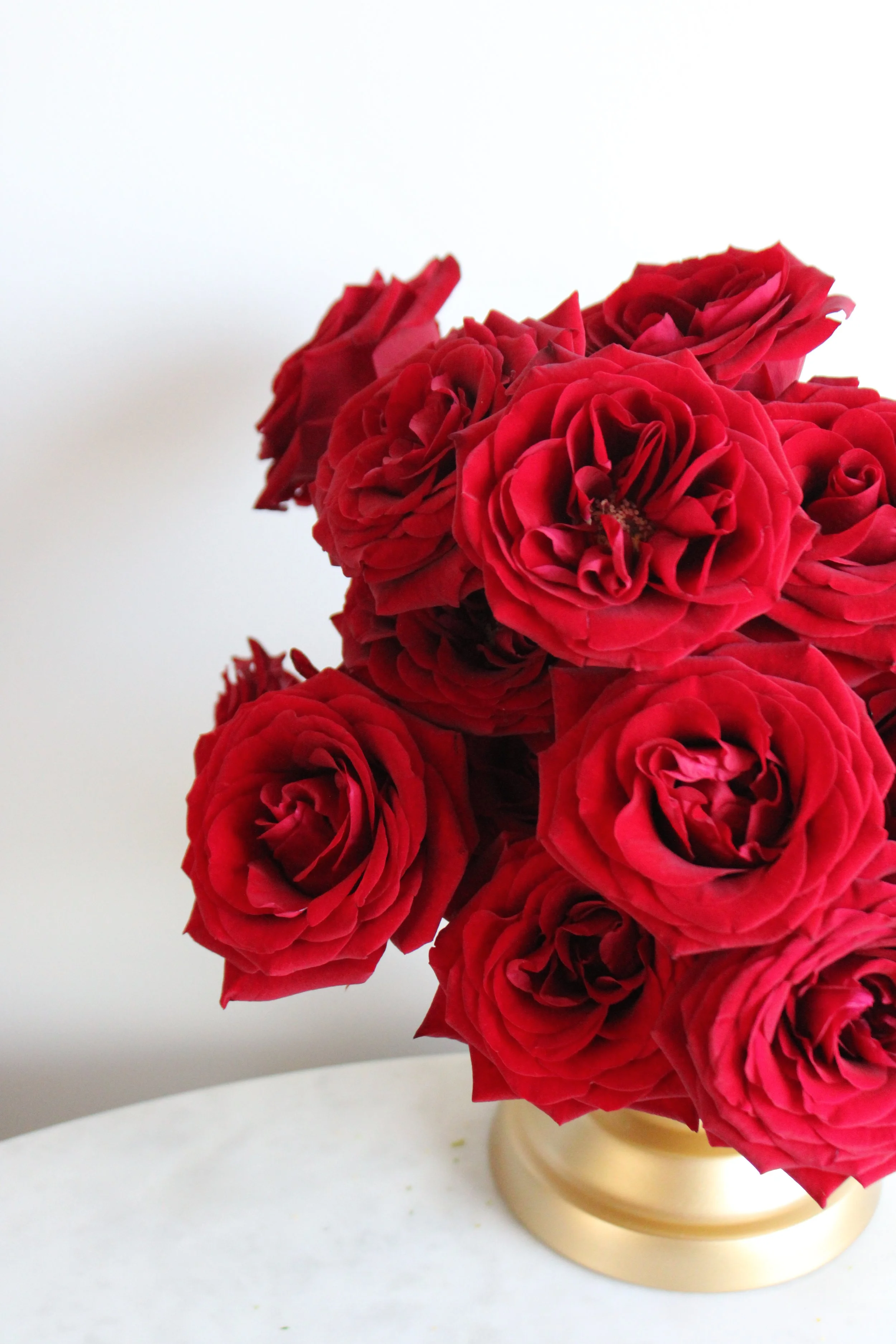 A bouquet of red roses in a gold-colored vase on a white surface with a plain white background.