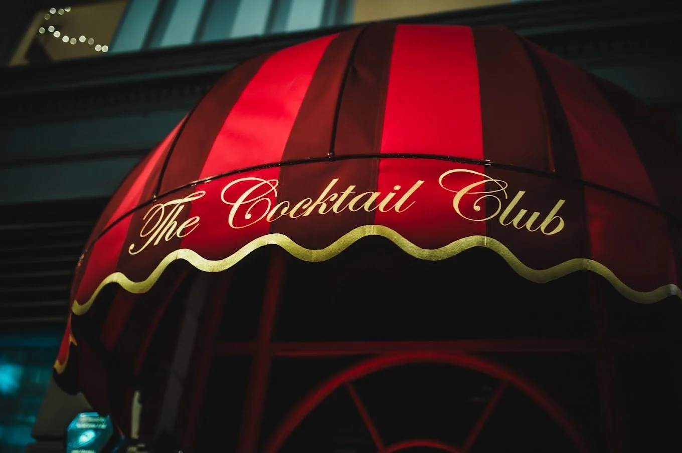 Close-up of a red and black striped canopy with the words "The Cocktail Club" written in cursive gold lettering.