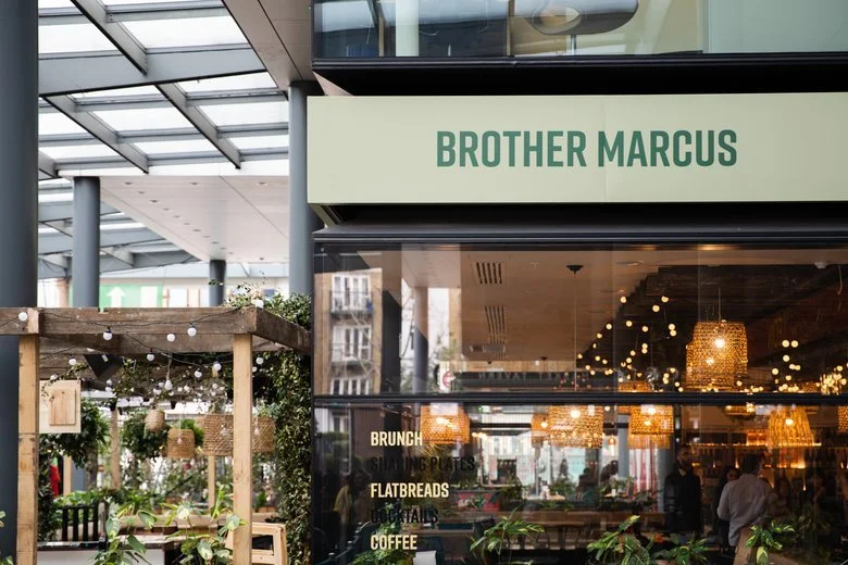 Outdoor area and restaurant named Brother Marcus with menu items like brunch, sharing plates, flatbreads, and coffee visible through large glass windows.