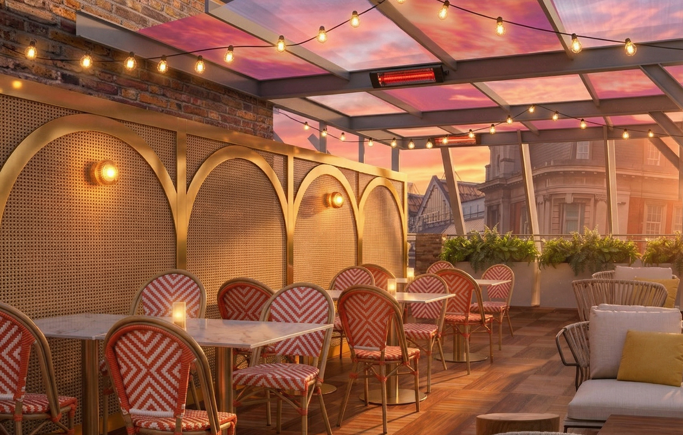 Night time rooftop terrace with string lights, ornate chairs with red and white patterned cushions, small tables, and a sunset sky
