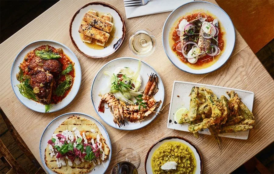 Assorted dishes including seafood, pasta, and vegetables on a wooden table with wine