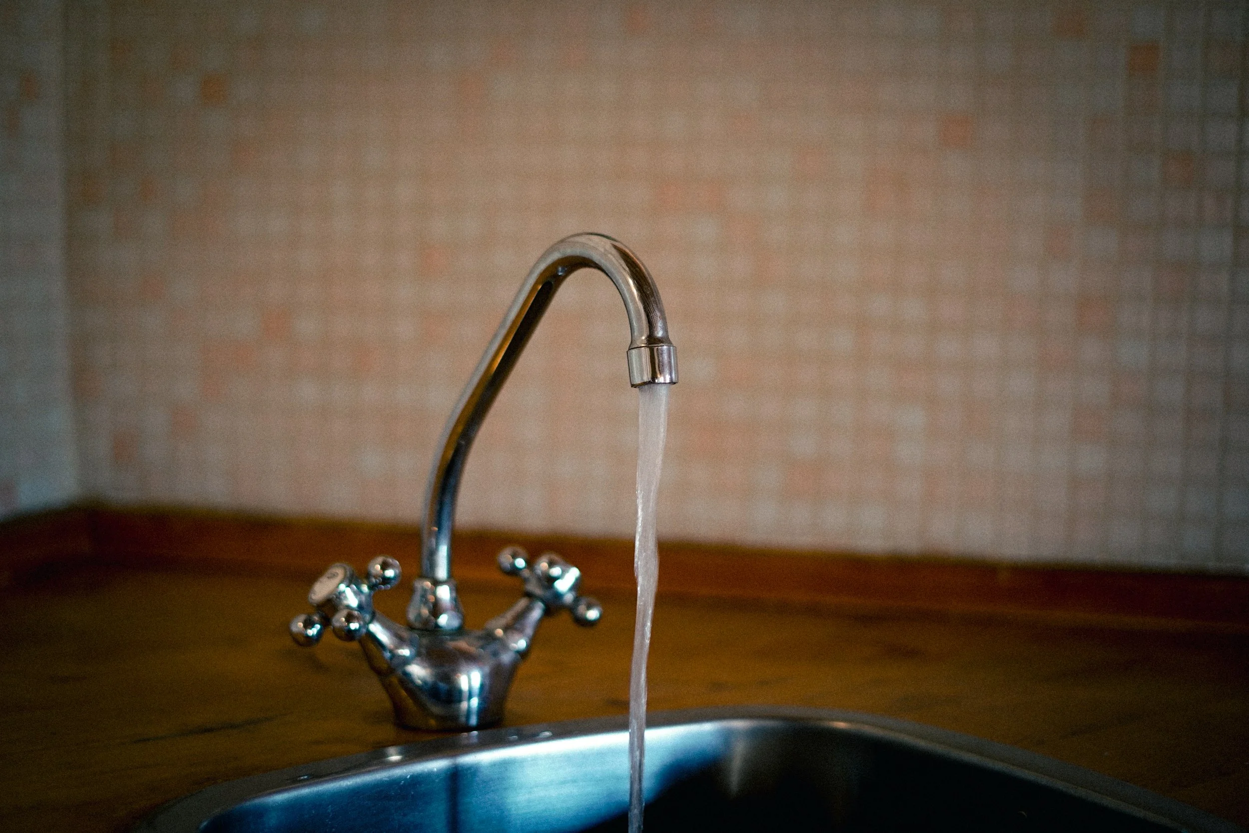 Ein Wasserhahn, aus dem Wasser fließt, über einem Spülbecken, vor einer Wand mit Mauerwerksmuster.