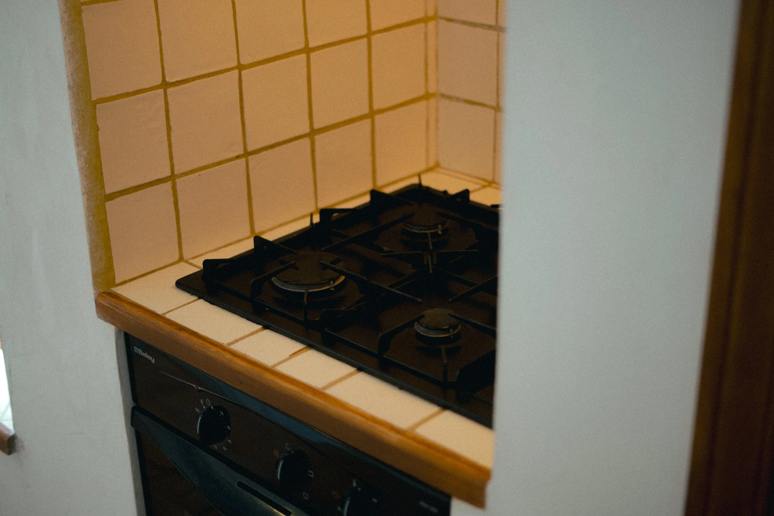 Ein Küchenherd mit zwei Gasflammen auf einer beige-weiß gefliesten Küchenarbeitsplatte.