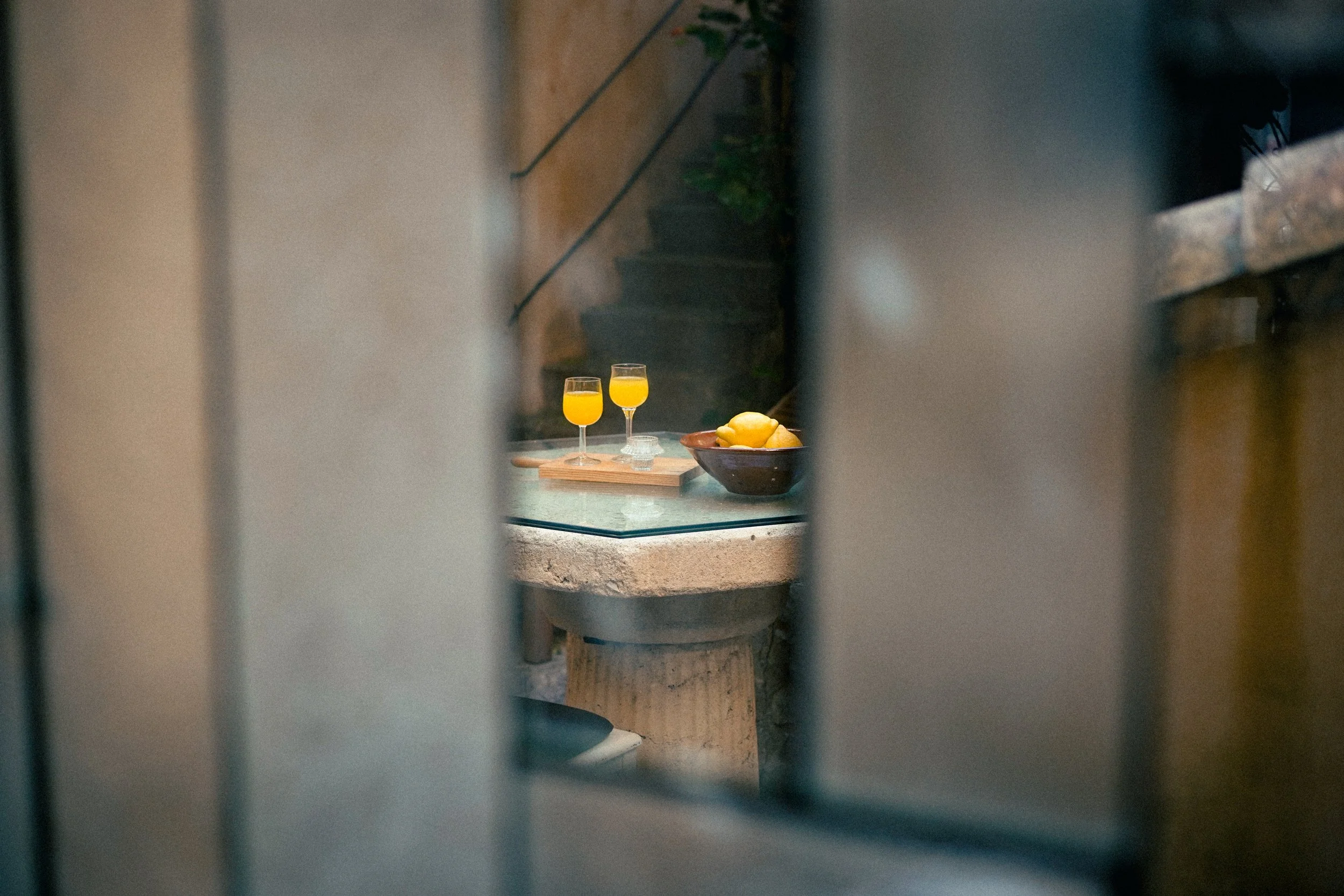 Blick durch einen Türspalt auf eine Küchentheke mit zwei Gläsern Orangensaft, einer Schale mit Zitronen und einem dunklen Topf im Hintergrund.