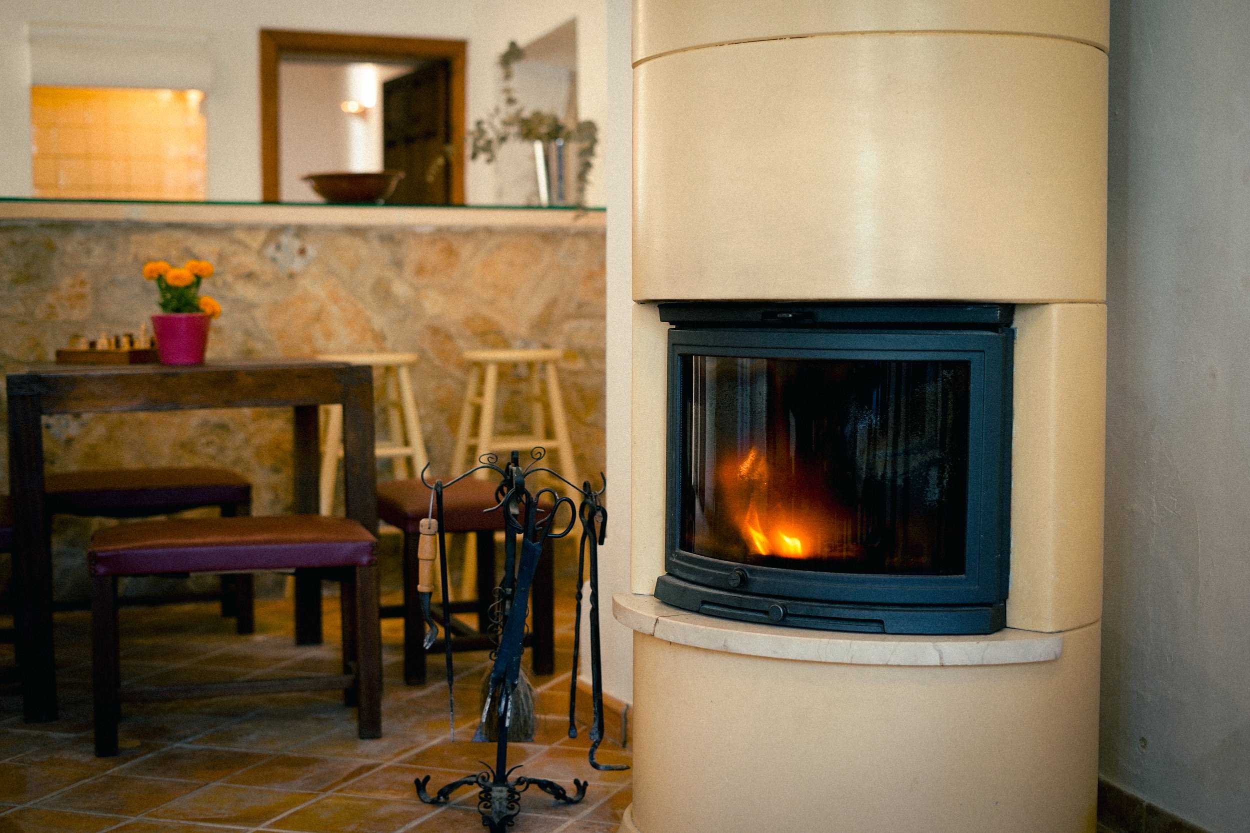 Ein Wohnzimmer mit einem Kamin, der Feuer hat, und einem Esstisch mit Stühlen, darunter Fliesenboden.