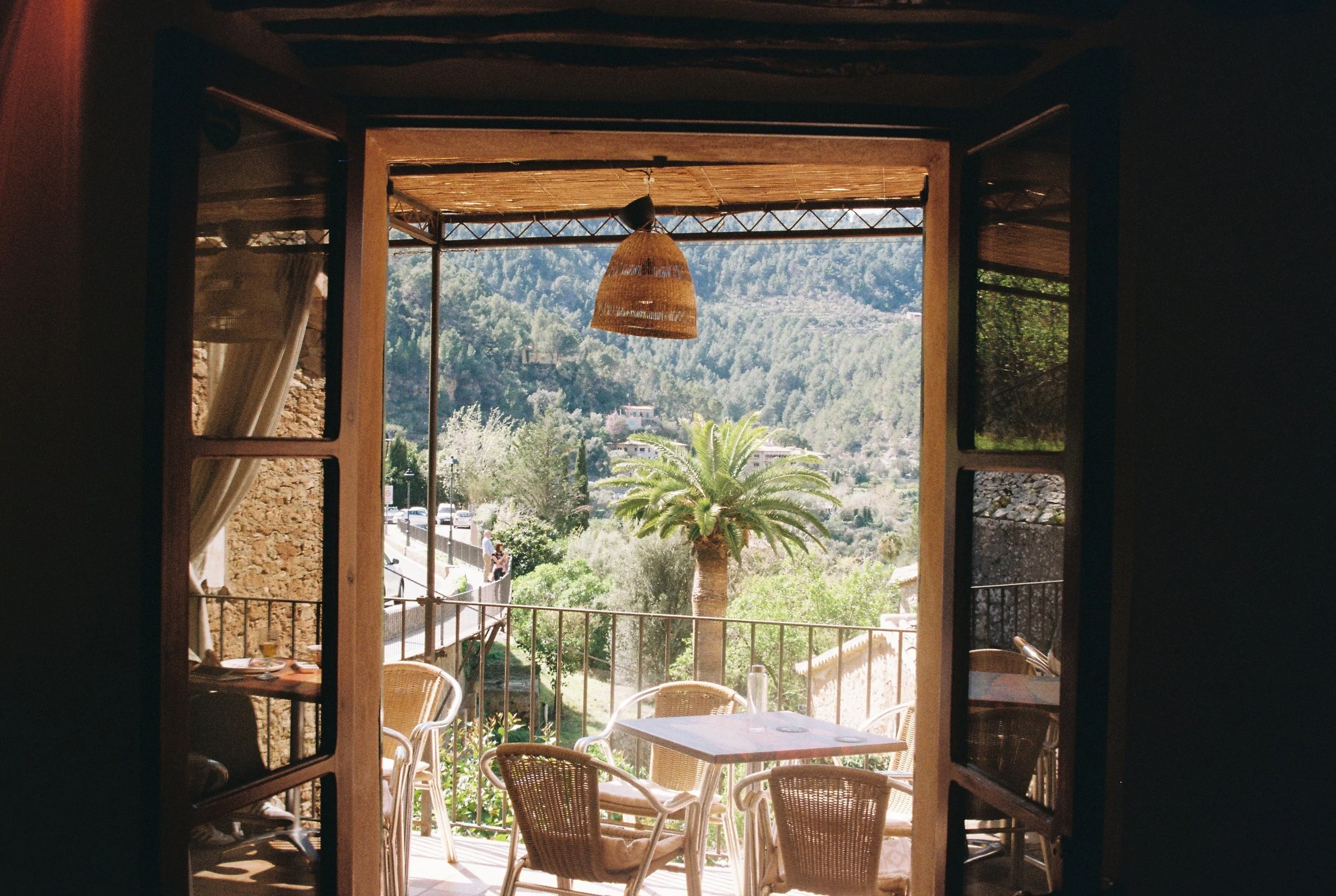Sicht auf einen Balkon mit Gartenmöbeln und Palmen, Blick nach draußen auf eine bewaldete Berglandschaft bei sonnigem Wetter.