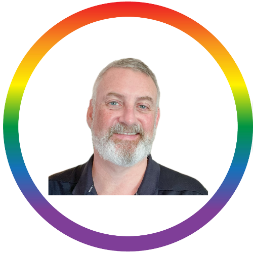 Portrait of a middle-aged man with a beard and short gray hair, wearing a dark collared shirt, smiling against a white background with a colorful circular border.