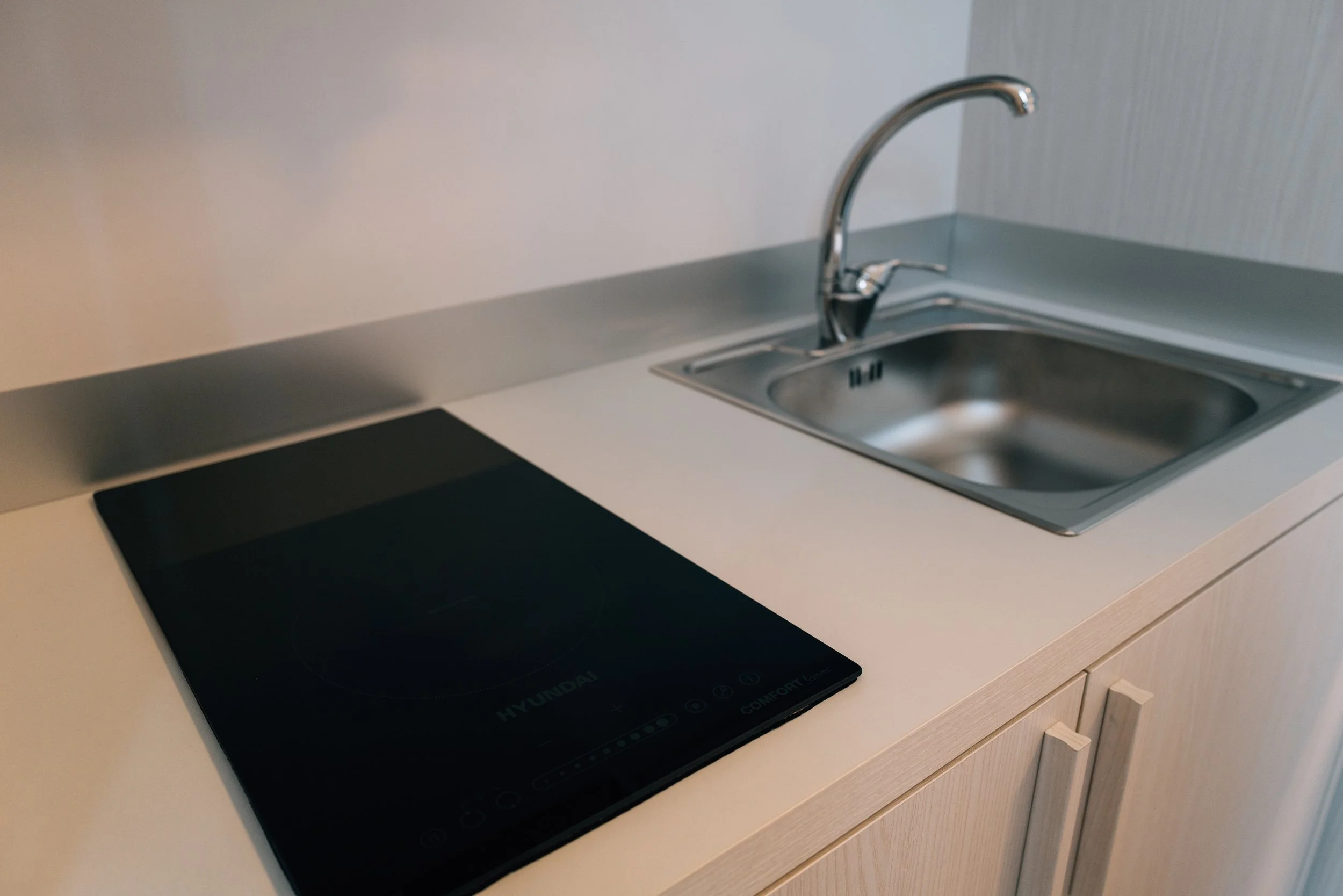 Angolo di una cucina con piano cottura a induzione nero e lavandino in acciaio inox