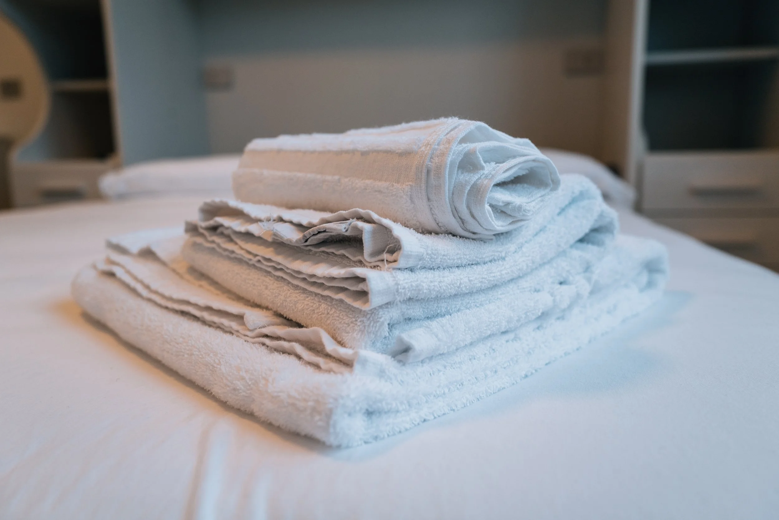Asciugamani bianchi piegati e impilati su letto, in una stanza