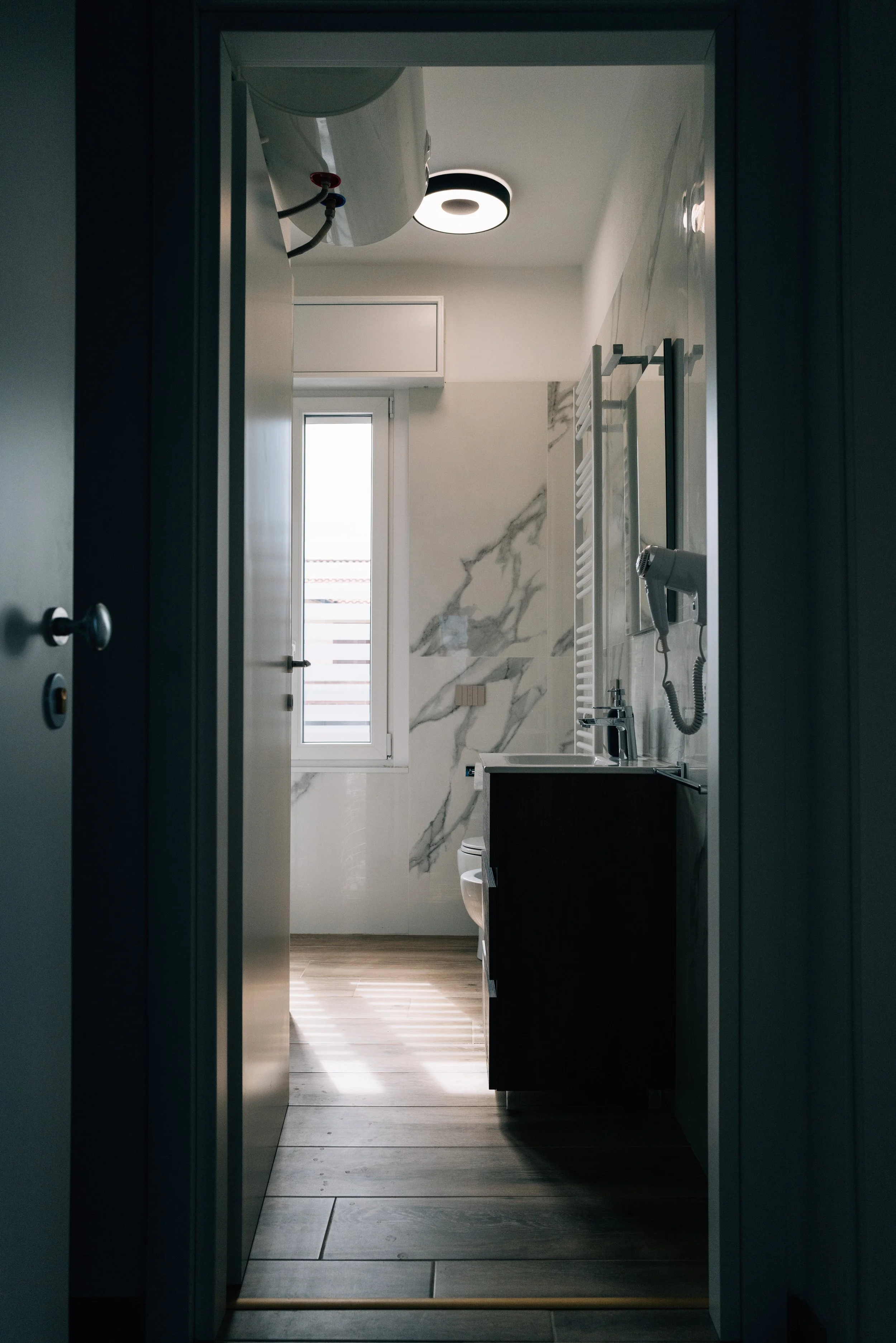 Interno di un bagno con pareti in marmo, finestra luminosa, lavabo, asciugacapelli e scaldasalviette