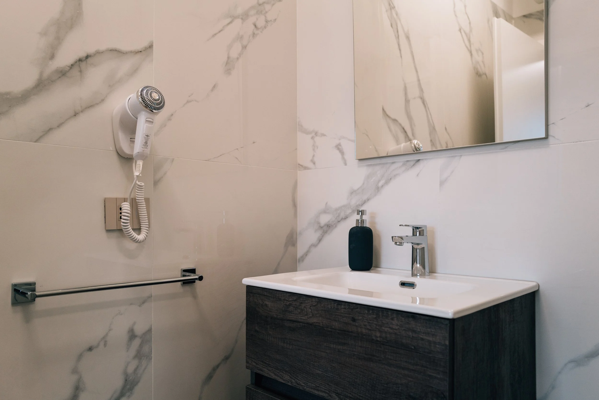 Bagno moderno con pareti in marmo e lavabo scuro con rubinetto, specchio e dispenser di sapone