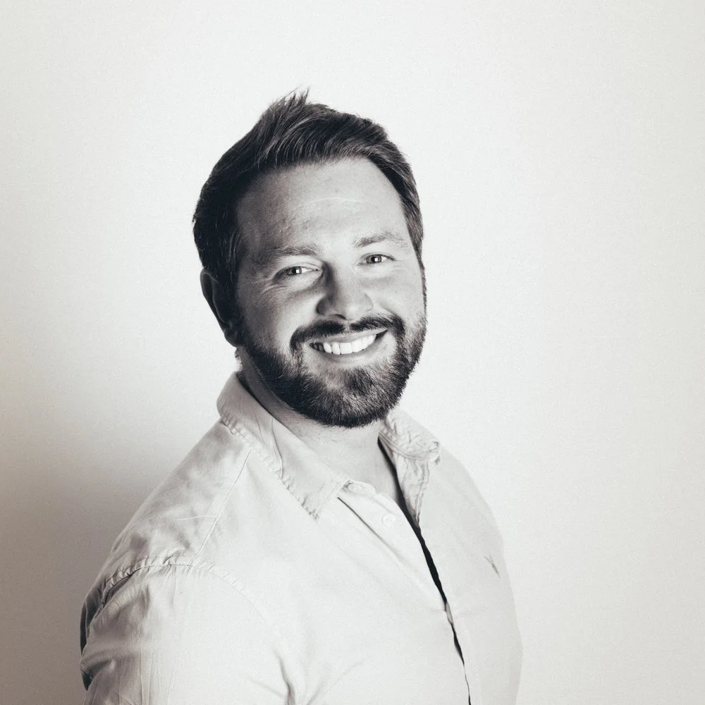 Black and white portrait of Rich Leigh, wearing a light-coloured button-up shirt, against a plain white background.