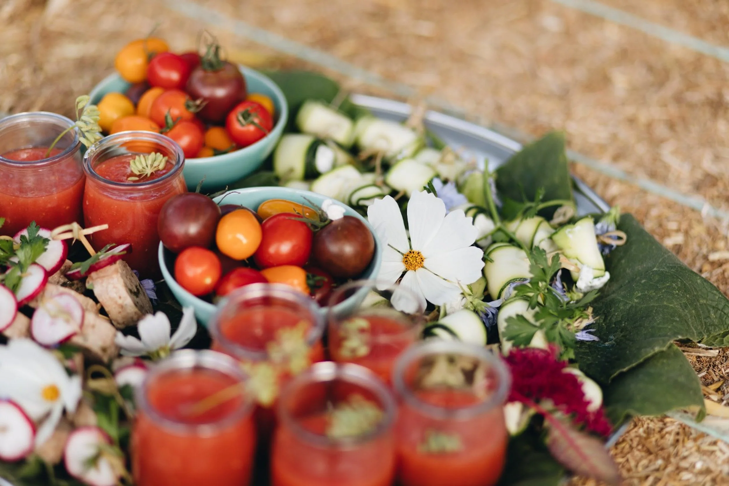 Een tafel met diverse verse groenten en kleine glazen met tomatensap, vers bloemen en bladeren.