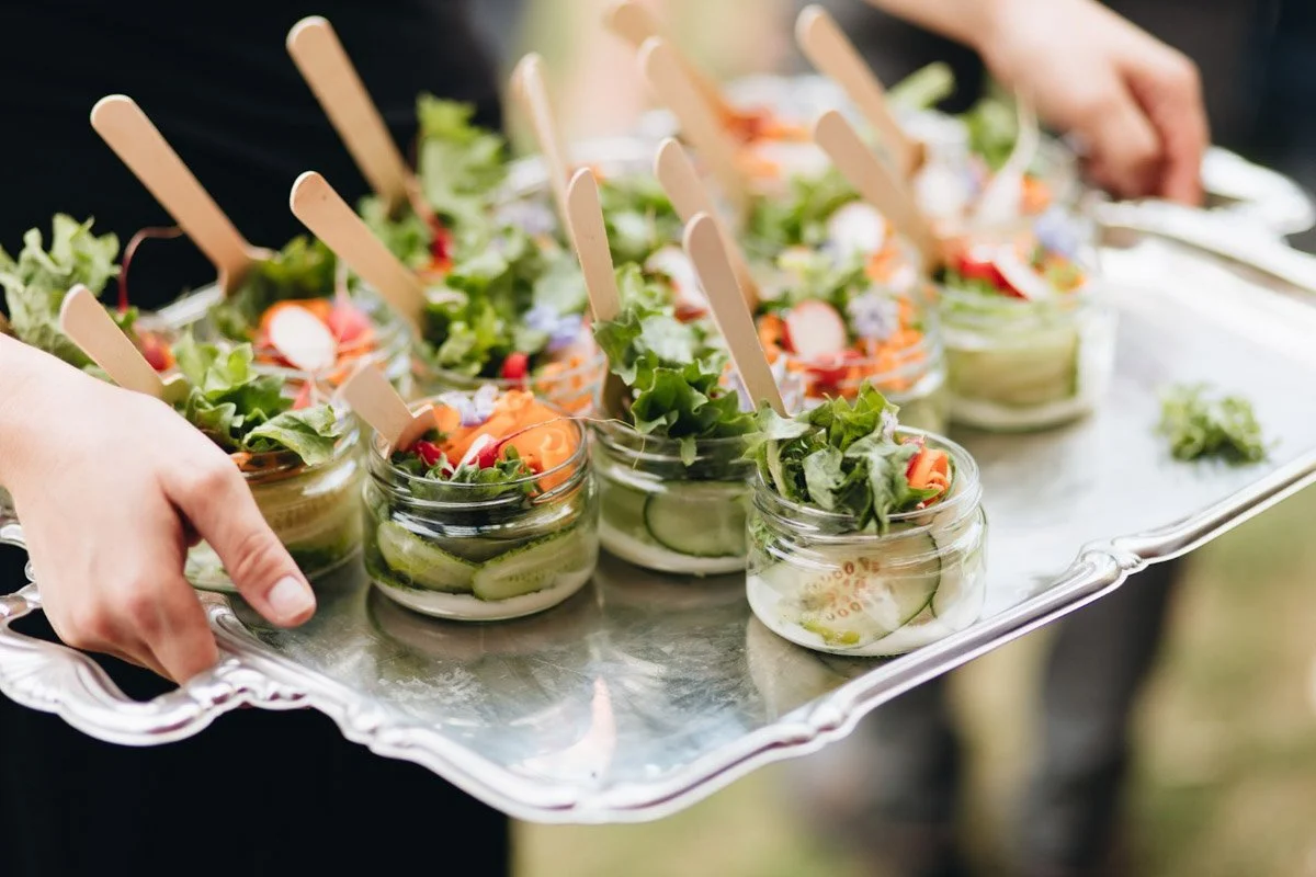 Gevulde glaasjes met salade en kleine houten lepels op een zilverkleurige dienblad.