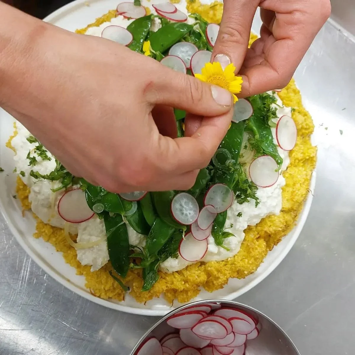 Personen voegen radijs en bloemen toe aan een gerecht met gekookte rijst en groenten.