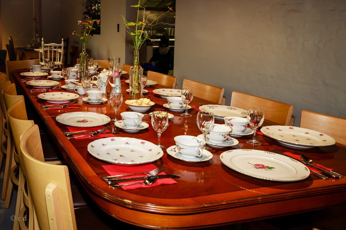 Een lange eettafel gedekt met bloemrijke servies, glazen en bestek, versierd met vazen met bloemen.