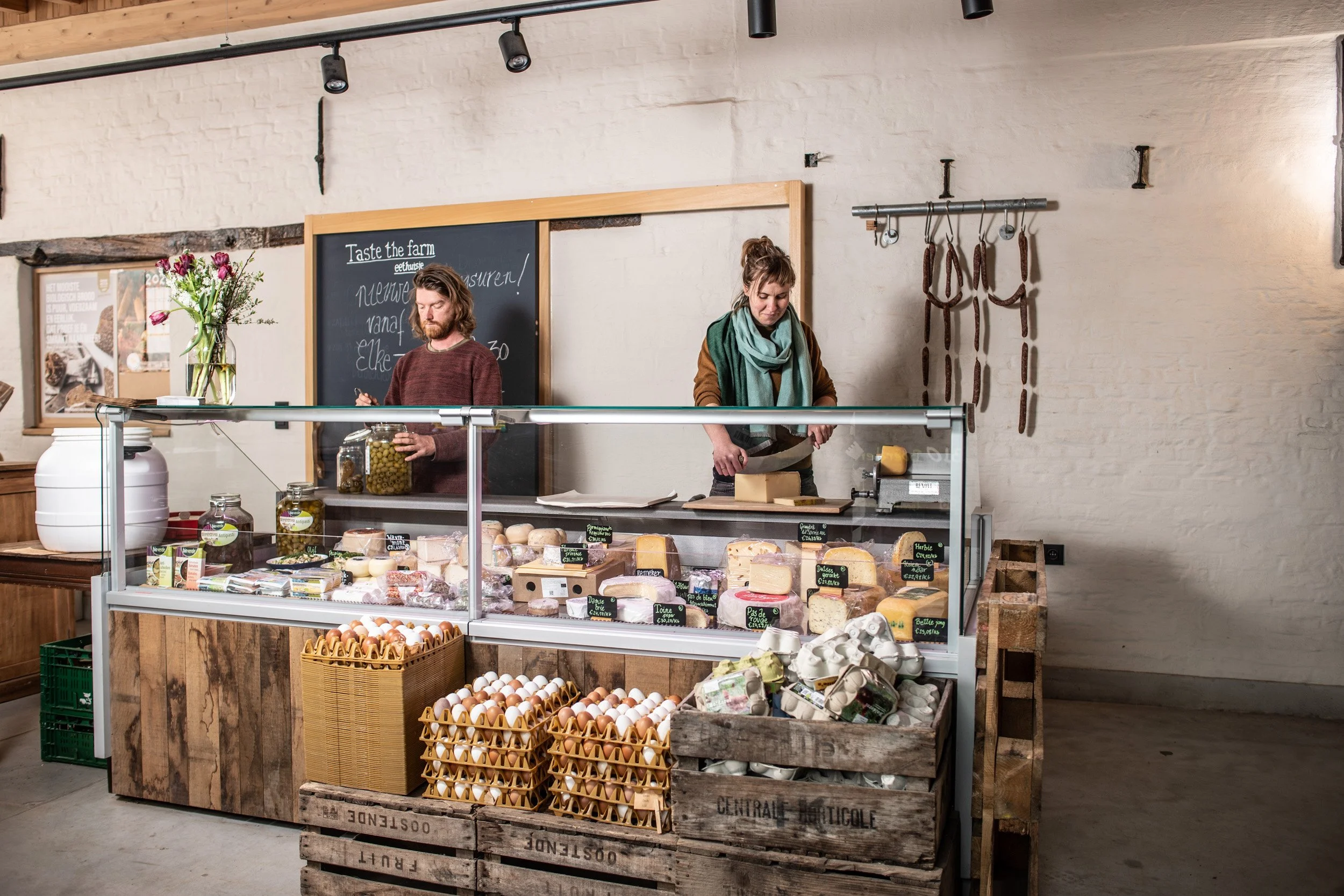 Vleeswaren en rauwe eieren uitgestald in een winkel met een houten toonbank en een zwart bord met witte tekst op de muur.