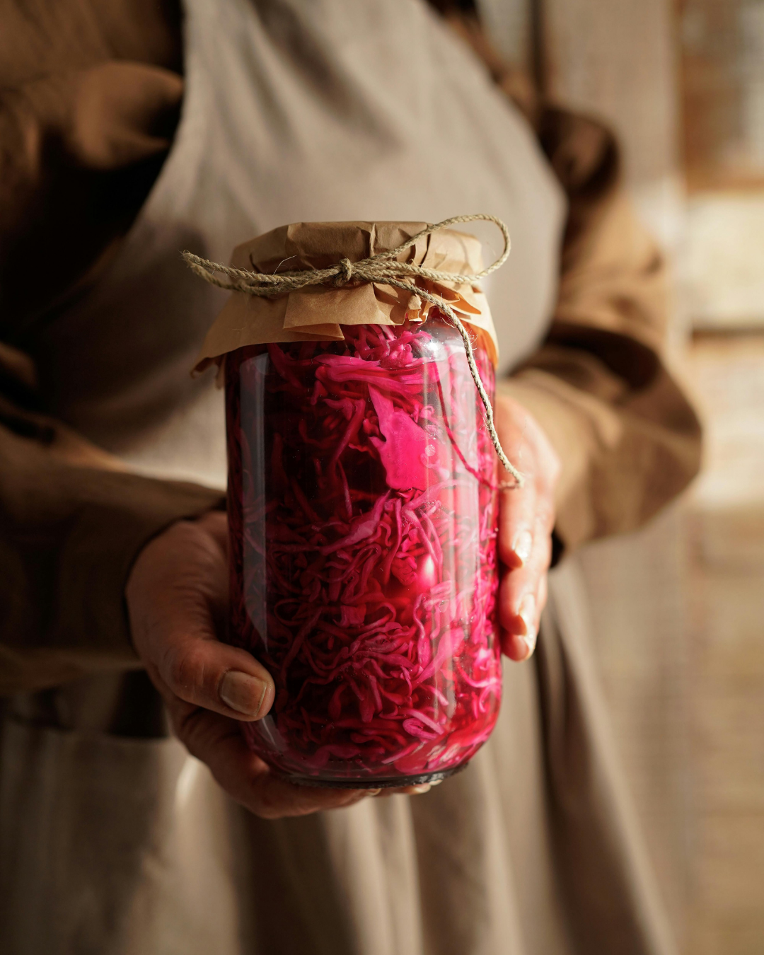 Hands holding a jar of pink pickled vegetables, showcasing traditional fermentation and food preservation techniques
