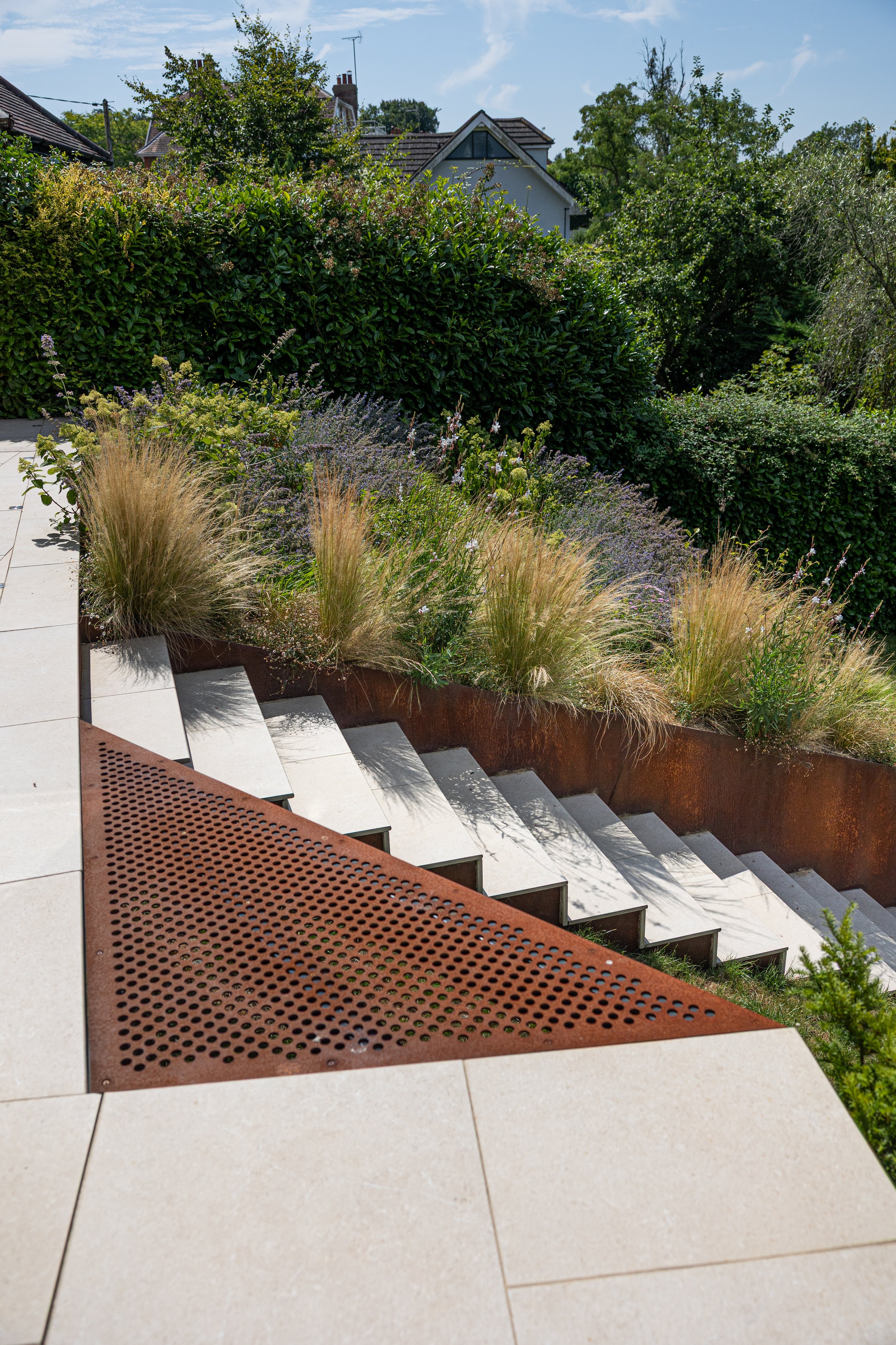 Balcombe sloping garden with corten steel sliced beds and a small steel bridge.