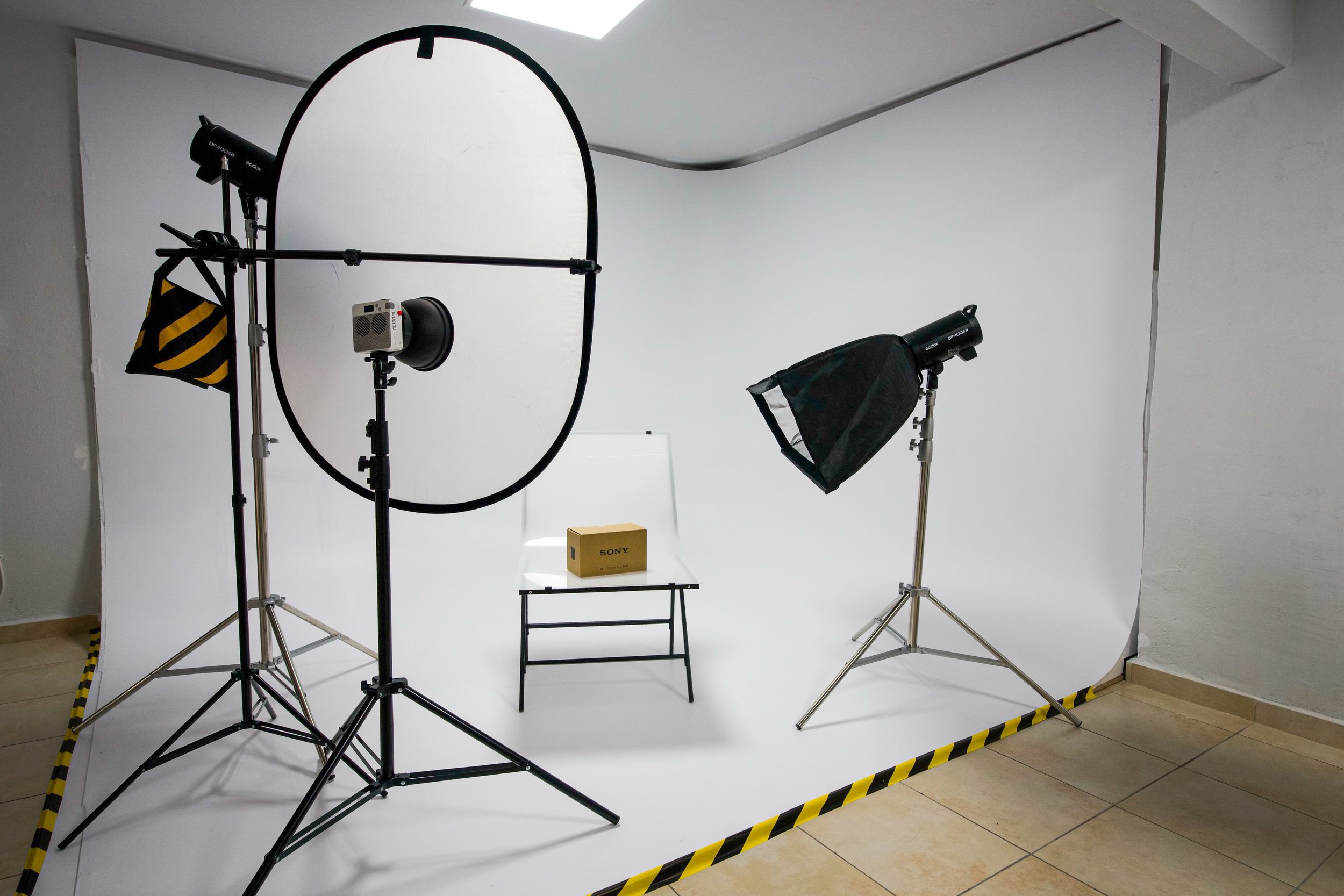 Photography studio setup with a white backdrop, professional lights, and equipment, including a Sony box on a small table.
