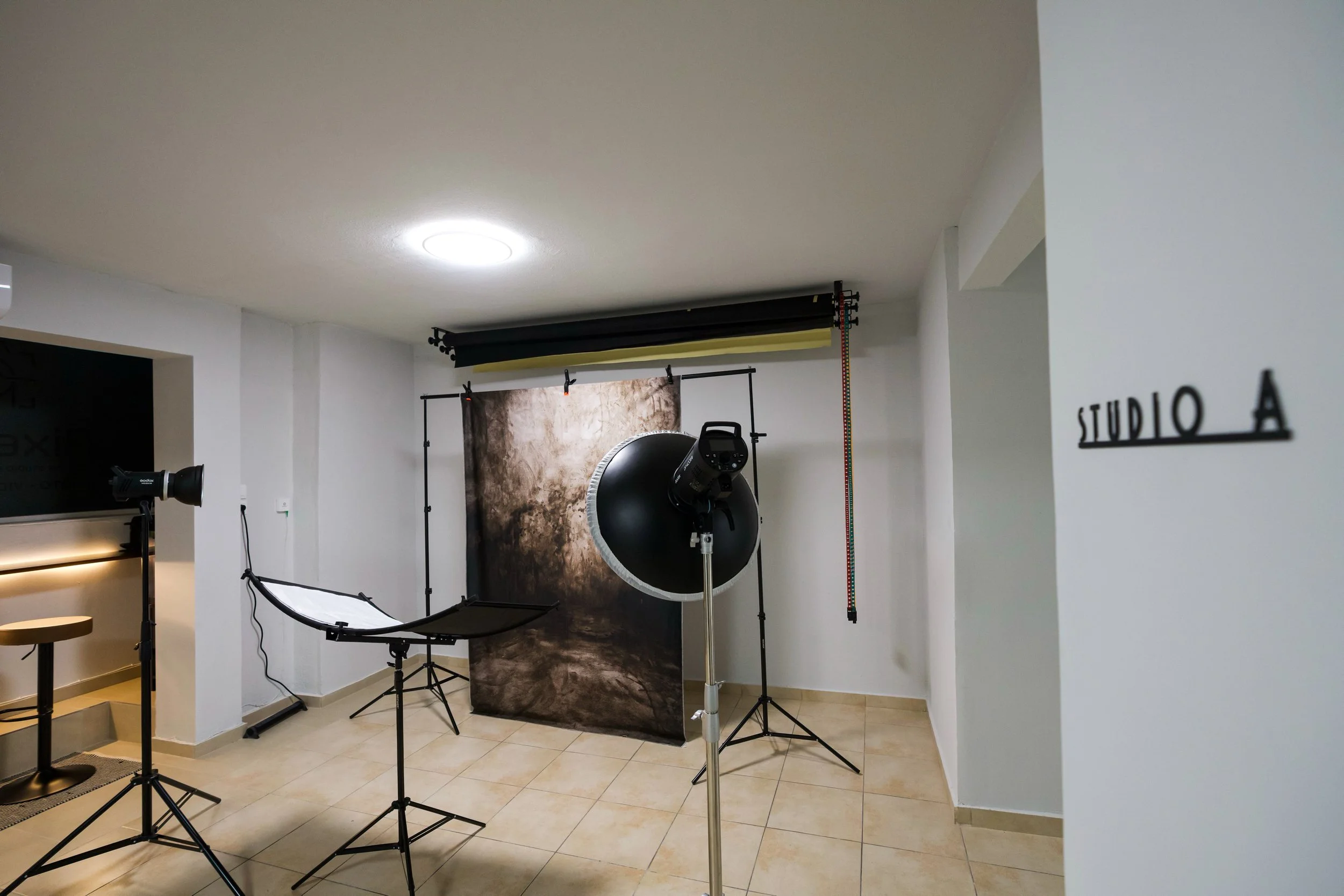 Photography studio setup with backdrops, lighting equipment, and a sign indicating Studio A, located in a room with beige tiled floors and white walls.