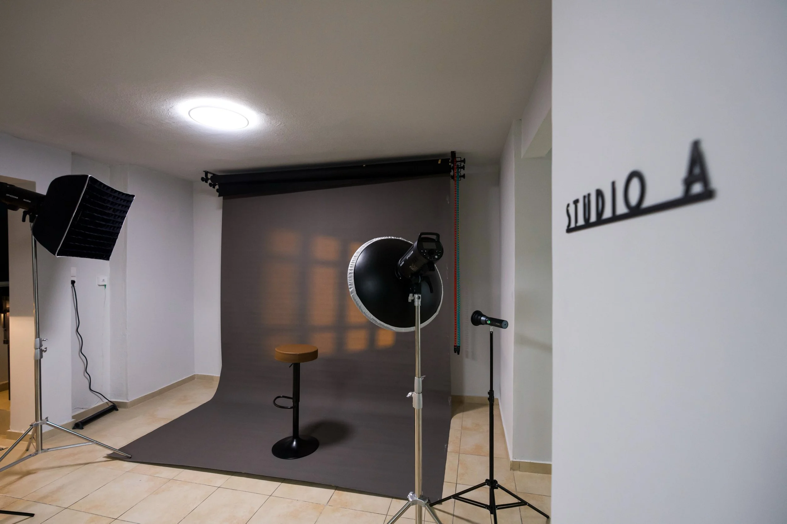A photography studio setup inside a room with a black backdrop, studio lighting, a stool, and a sign on the wall that reads 'STUDIO A'.