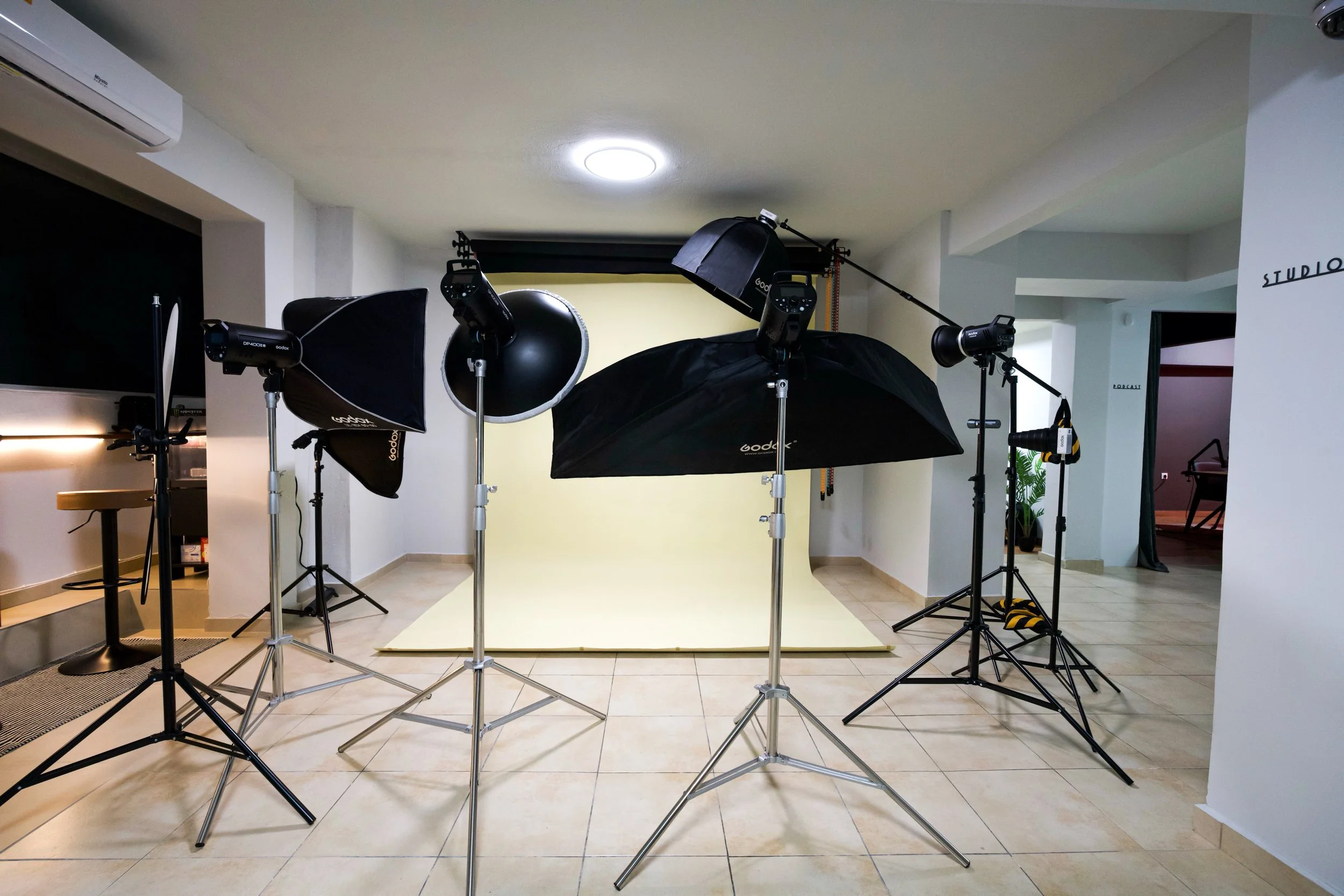 Photography studio setup with black umbrellas and lighting equipment in front of a yellow backdrop.