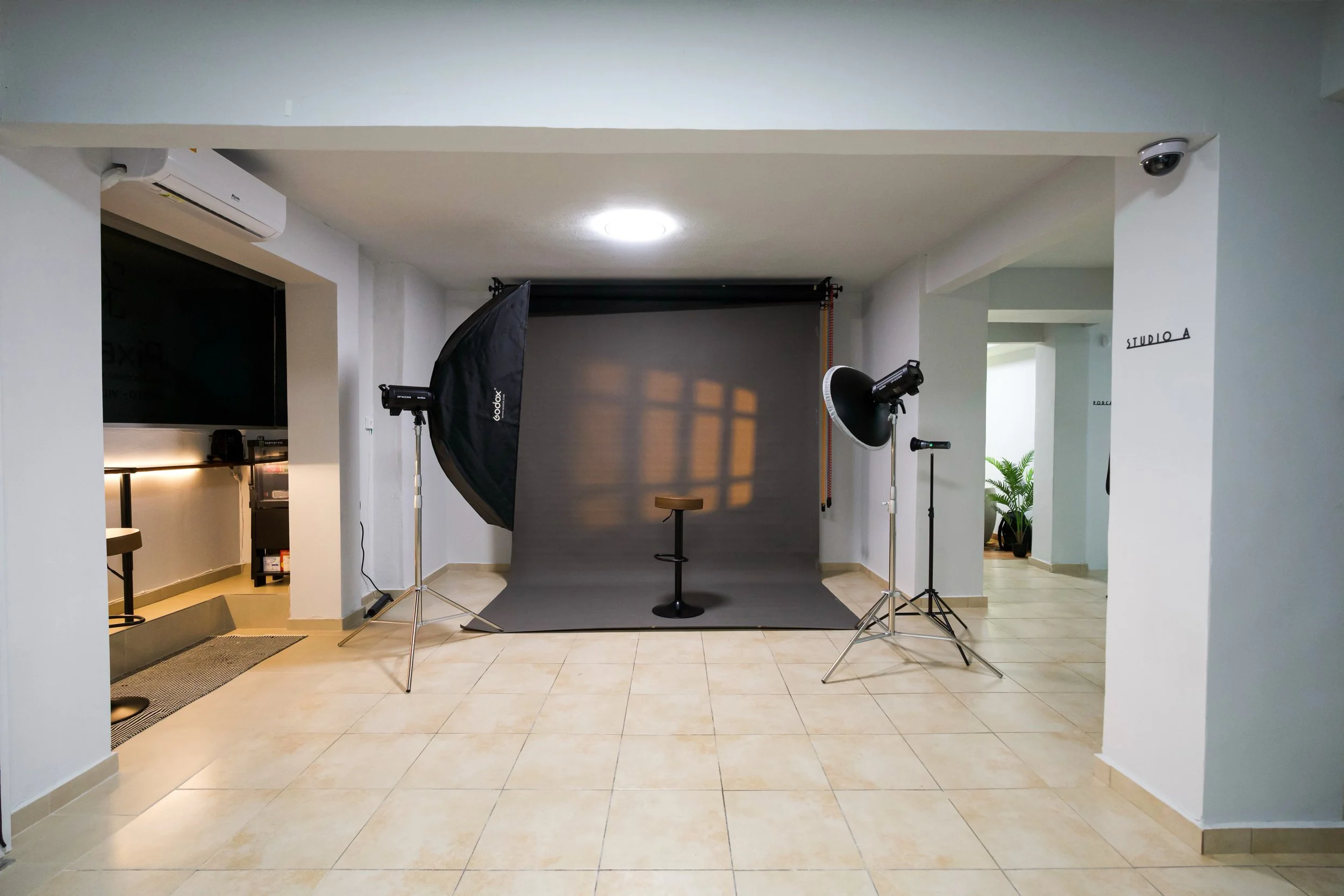 Photography studio with a black backdrop, professional lighting, and a stool, set up in a room with tiled floors, white walls, and a sign reading 'STUDIO A' on the wall.