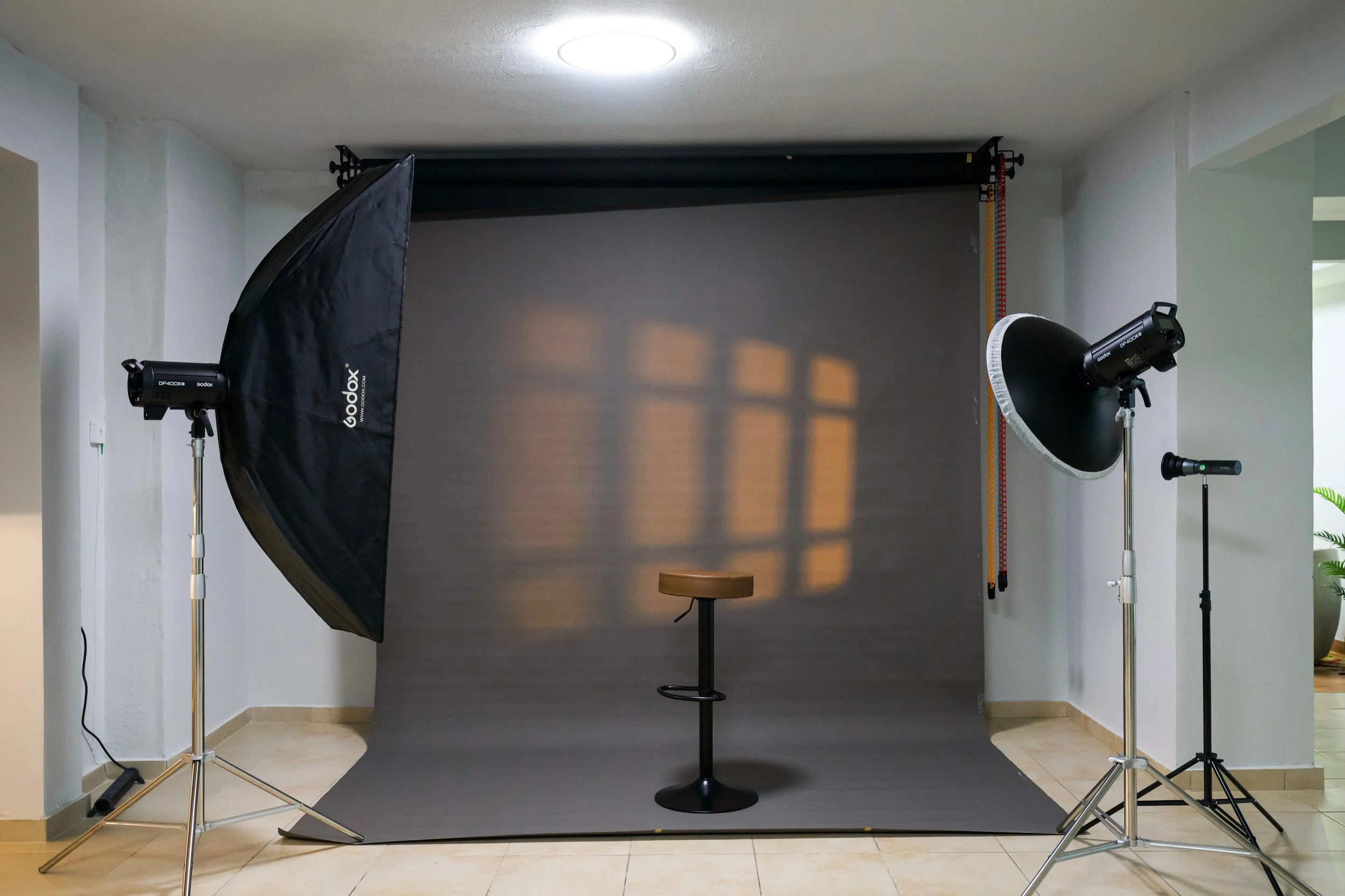 Photography studio setup with a backdrop, two softbox lights on stands, and a stool in front of the backdrop.