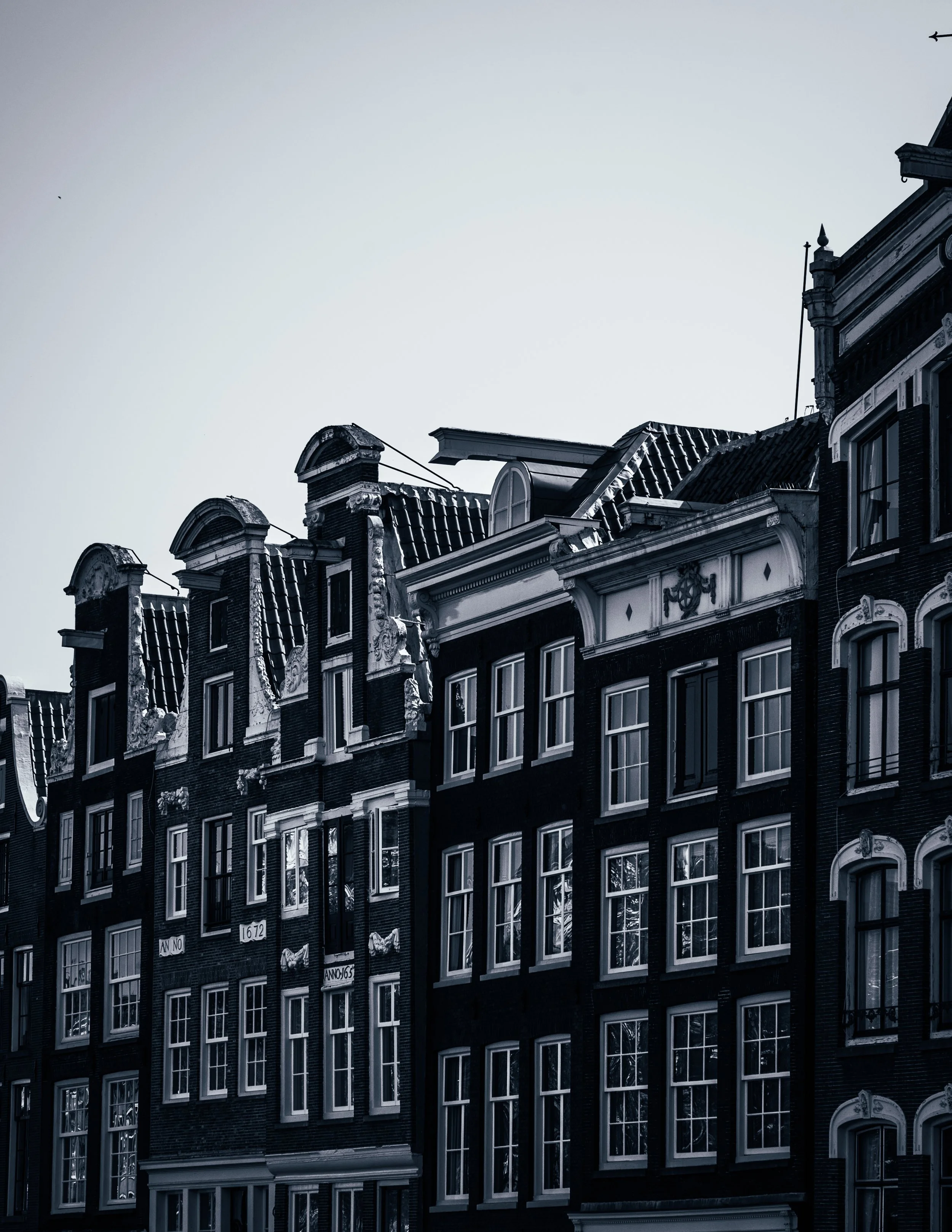 Black and white photograph of historic European-style buildings with ornate gables and multiple windows, under a clear sky.